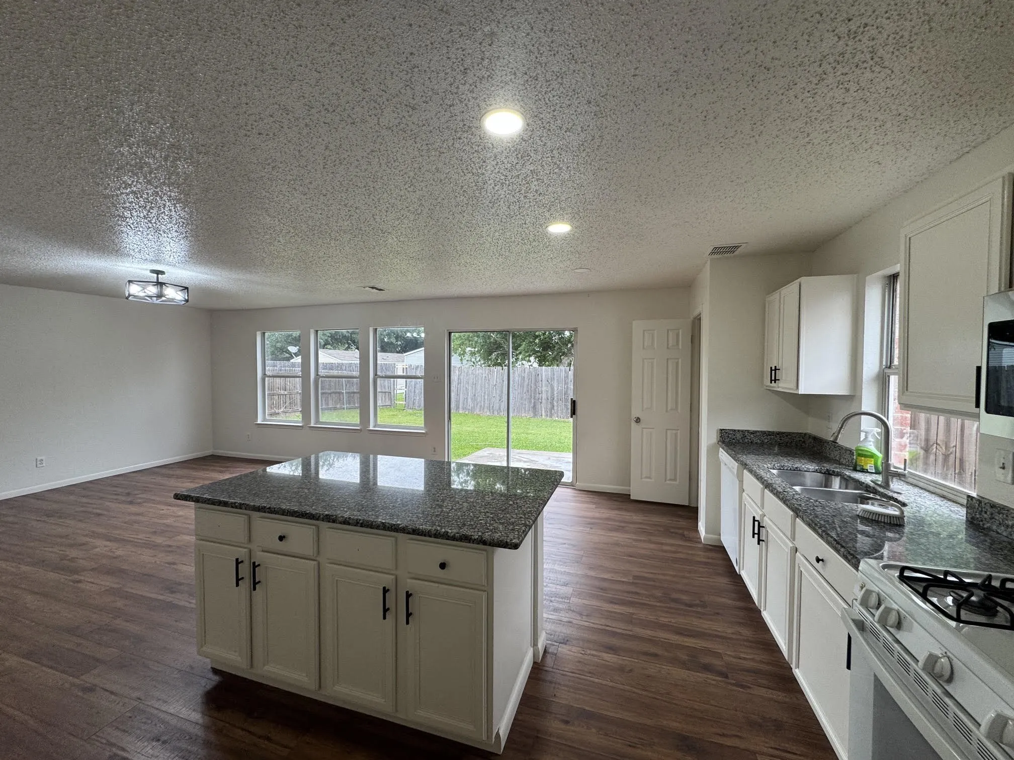 Open-concept kitchen and living area featuring wood-finish flooring, recessed lighting, and a kitchen island with stone countertops