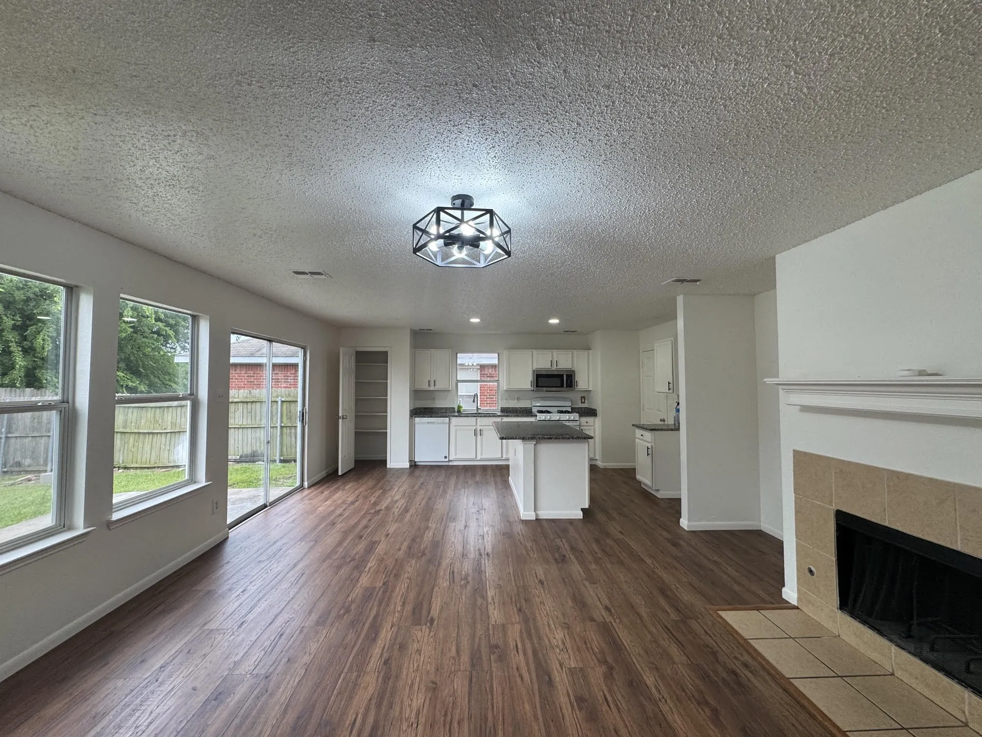 Open-concept living area featuring wood-finish flooring, a tiled fireplace, and a modern geometric ceiling light fixture