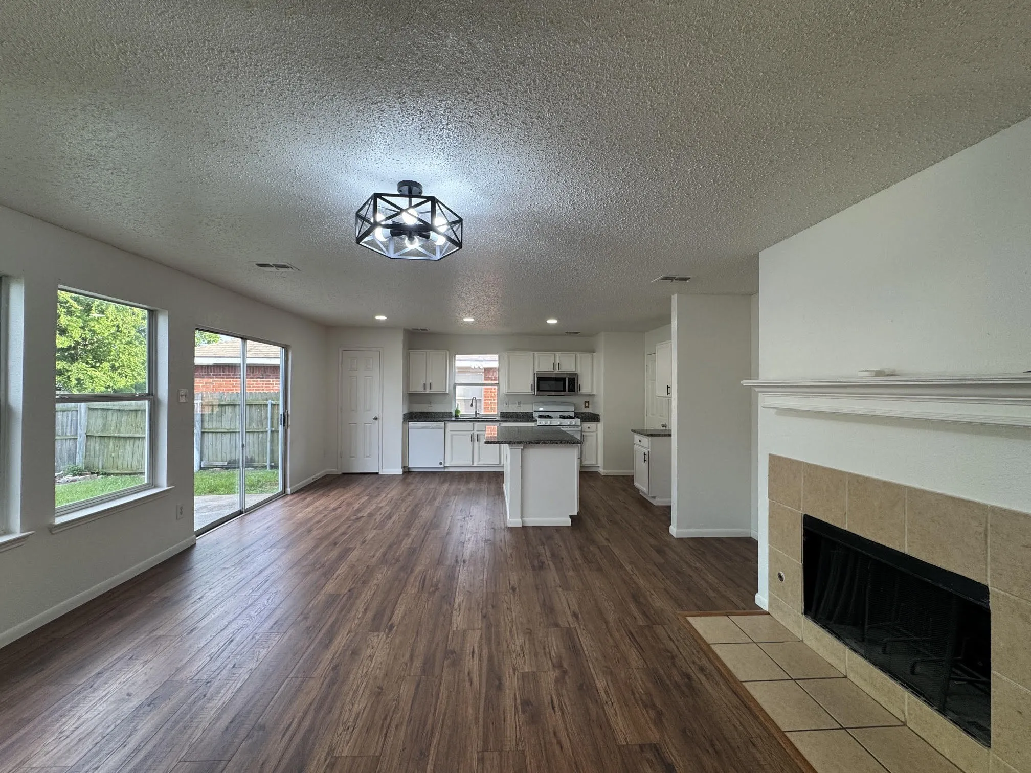 Spacious interior featuring wood-finish flooring, a contemporary ceiling light fixture, and white walls