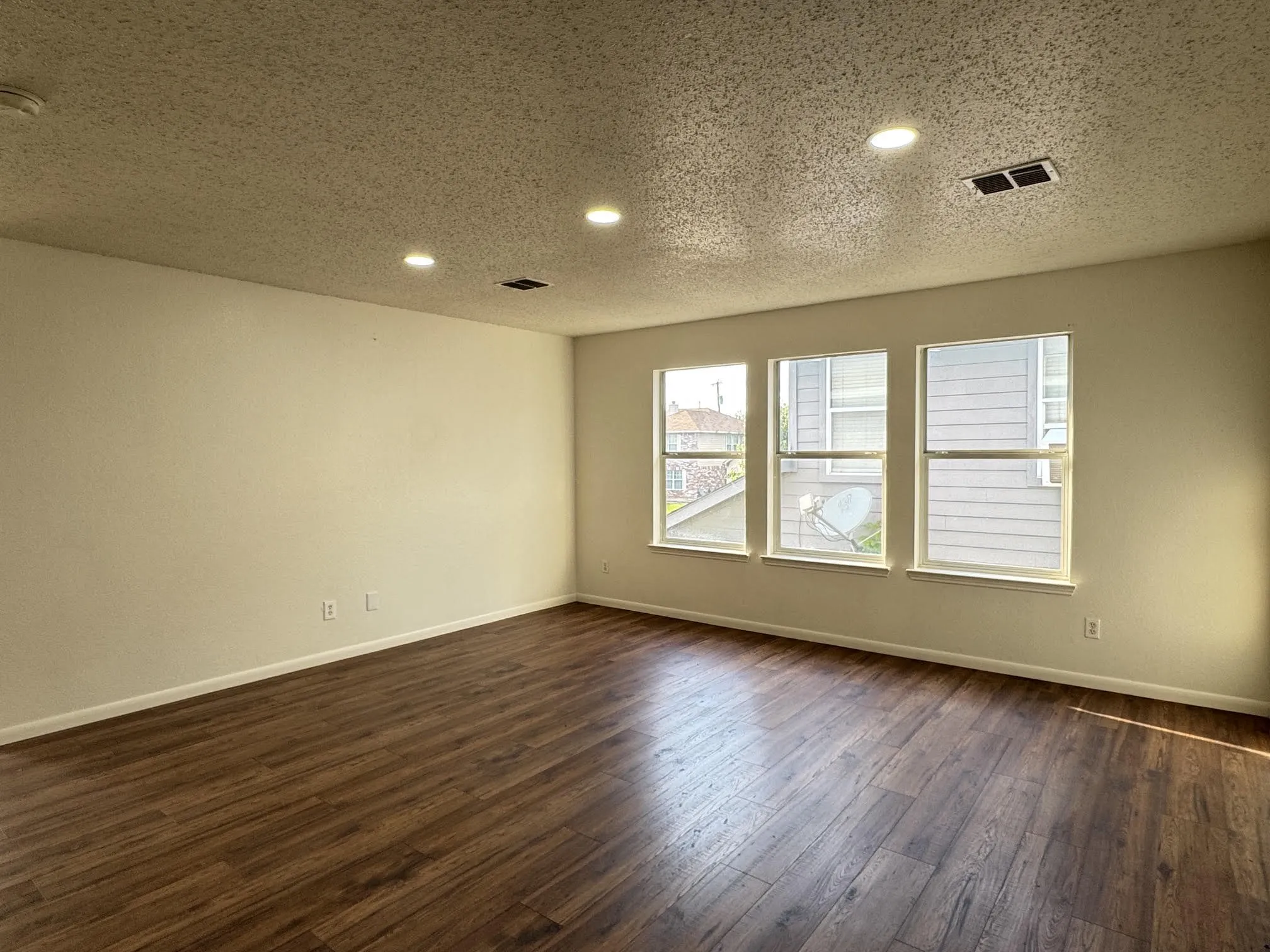 Spacious room featuring wood-finish flooring, recessed ceiling lighting, three windows, and light-colored walls