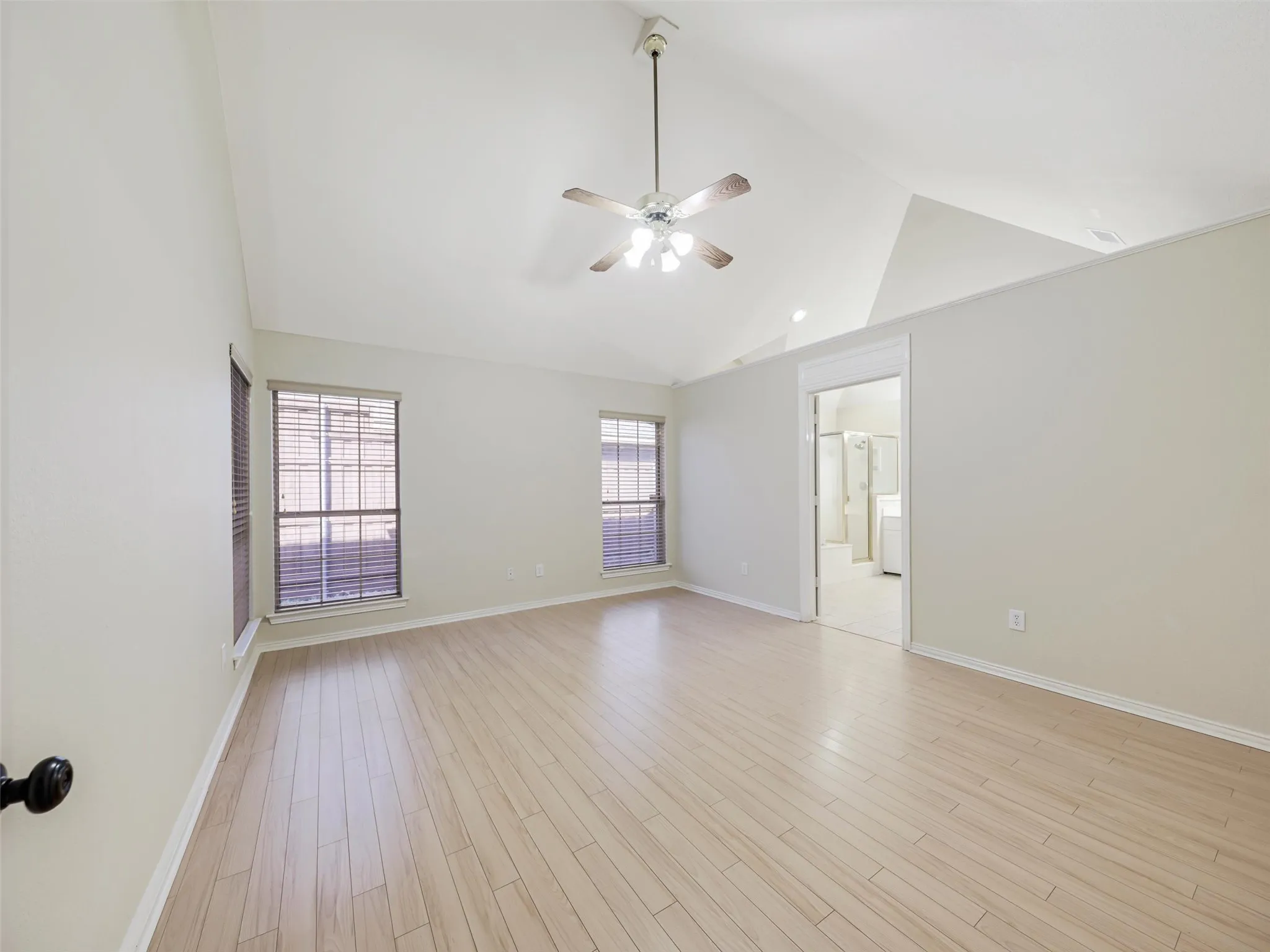 Vaulted ceiling with a ceiling fan, wood-finish flooring, and multiple windows with blinds