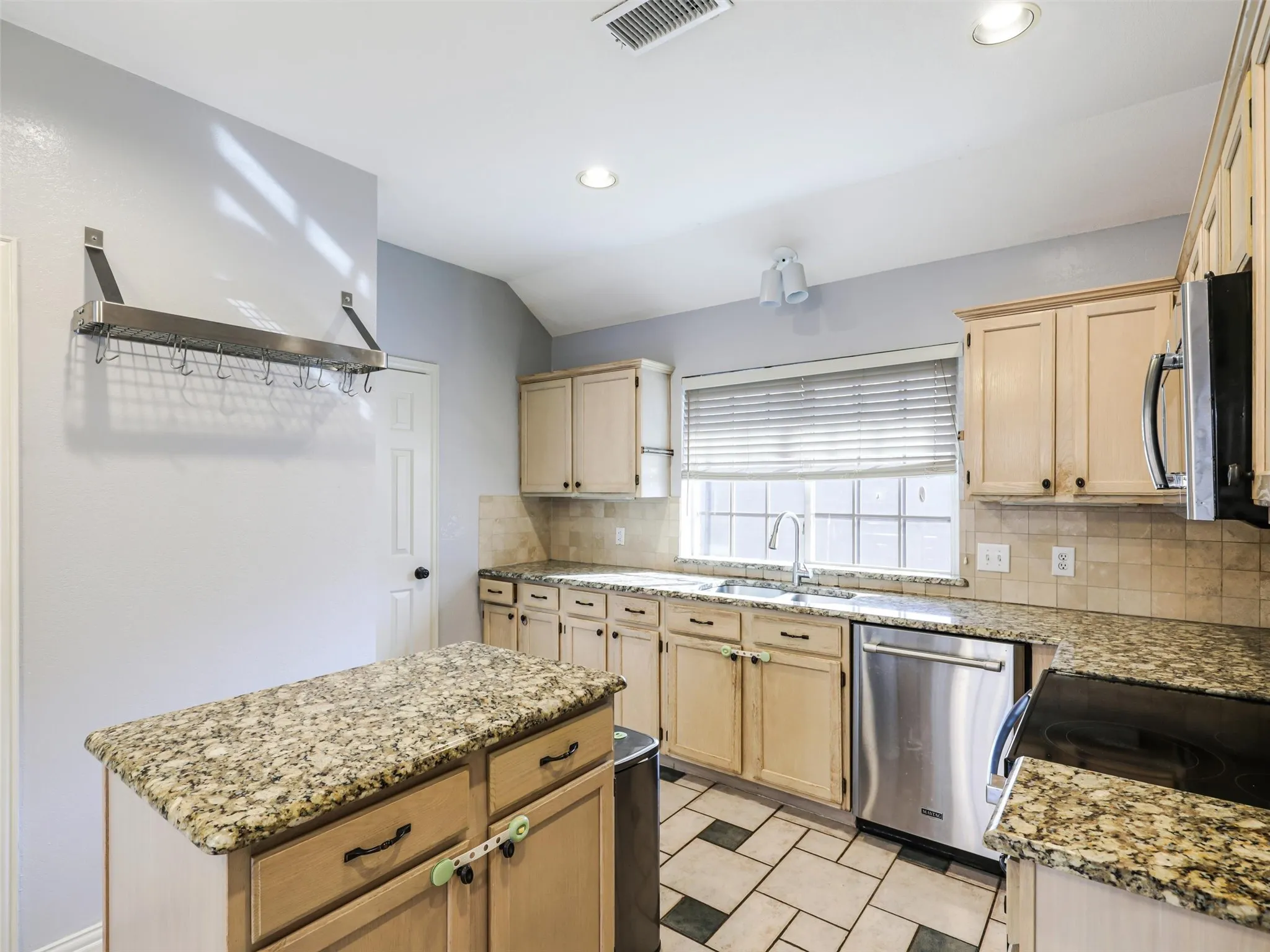 Kitchen featuring wood cabinetry, a center island with a granite countertop, stainless steel appliances, and tile flooring