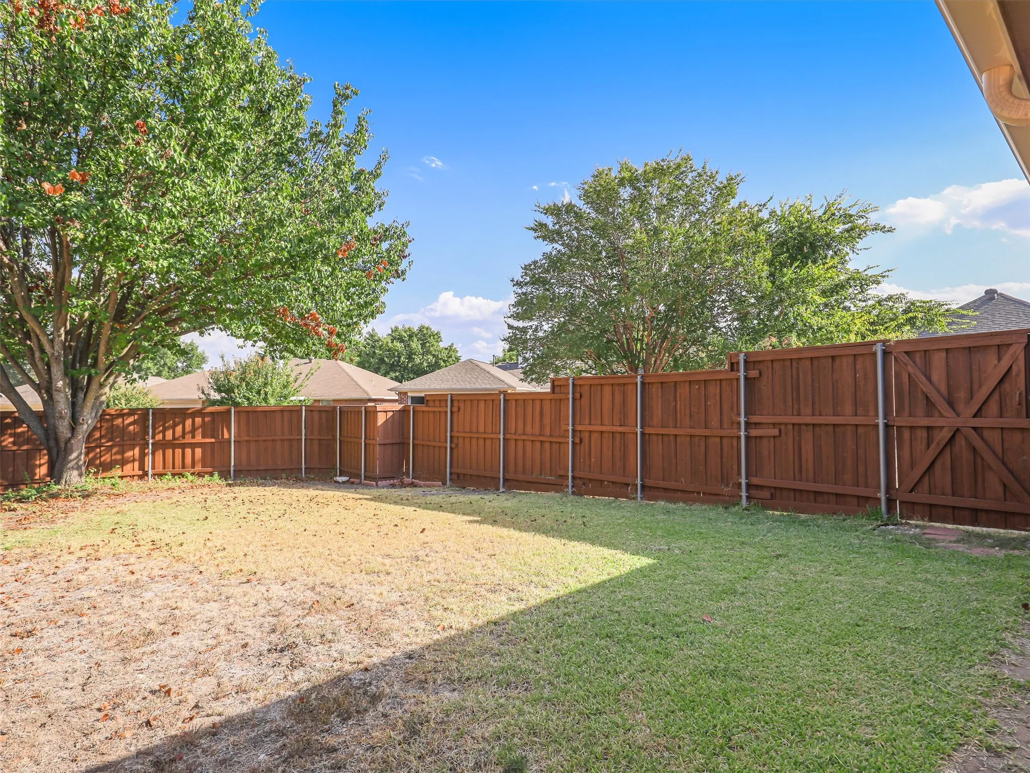 Fenced backyard featuring a wood privacy fence, mature trees, and a grass lawn