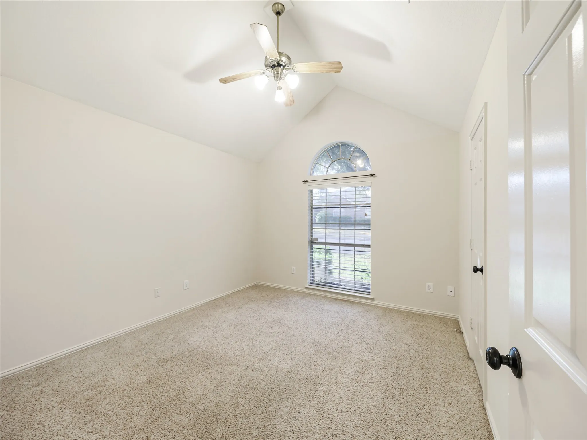 Vaulted ceiling, ceiling fan with light fixture, arched transom window, louvered blinds, and neutral carpeting