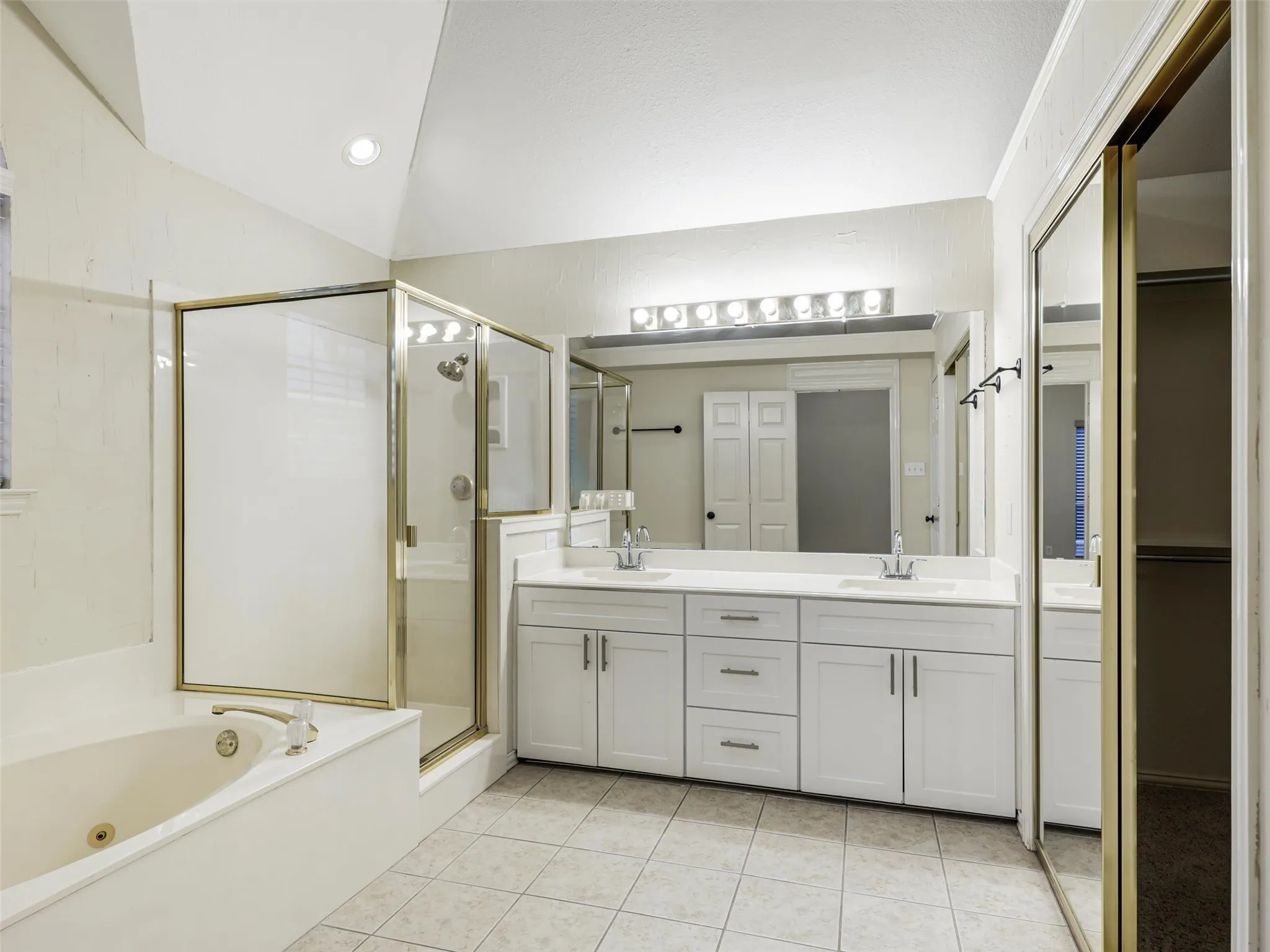 Dual vanity with undermount sinks, separate shower enclosure, built-in bathtub, mirrored closet doors, and tile flooring