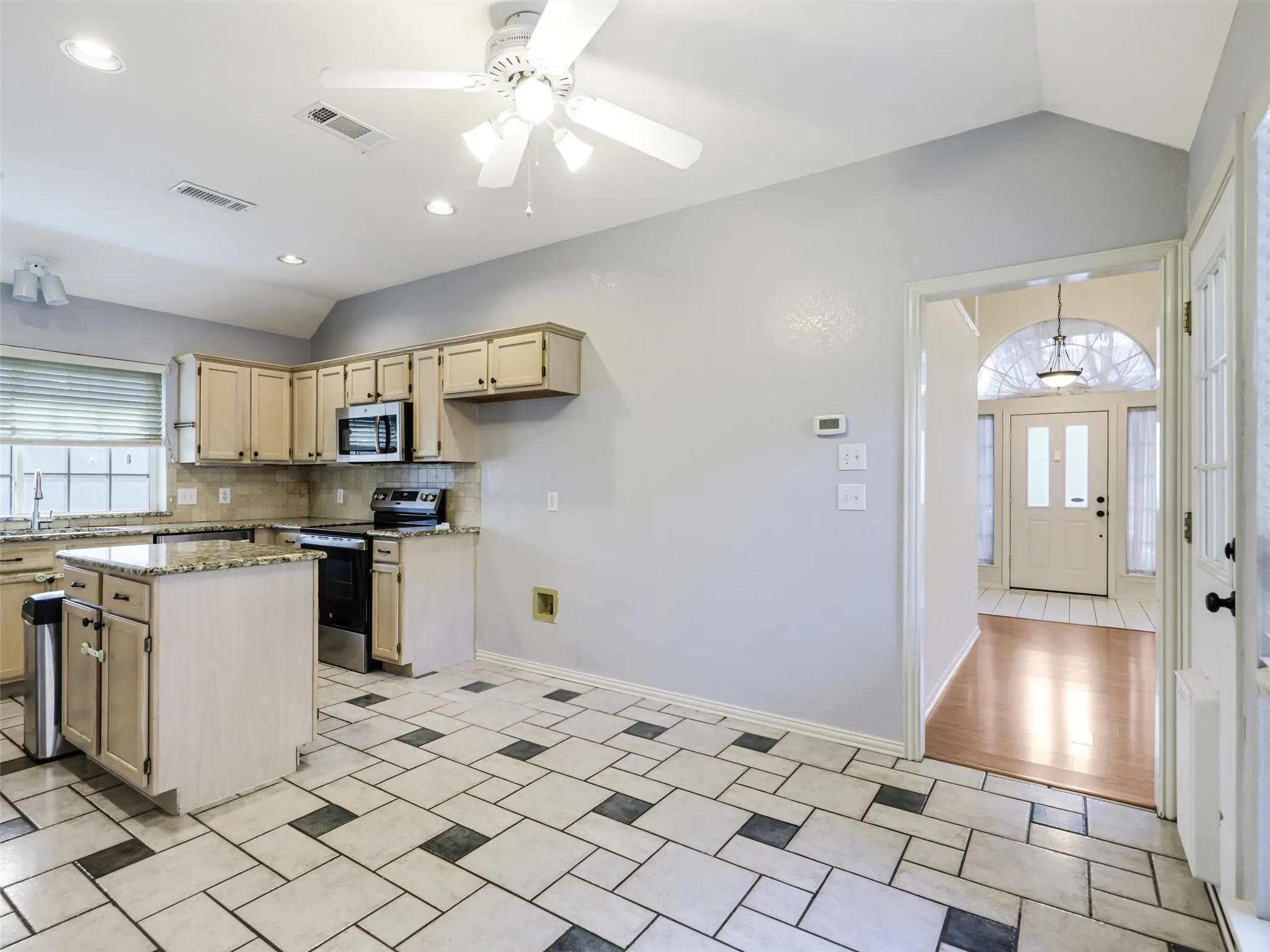 Kitchen with vaulted ceiling, recessed lighting, ceiling fan, tile flooring, and a kitchen island with stone countertops