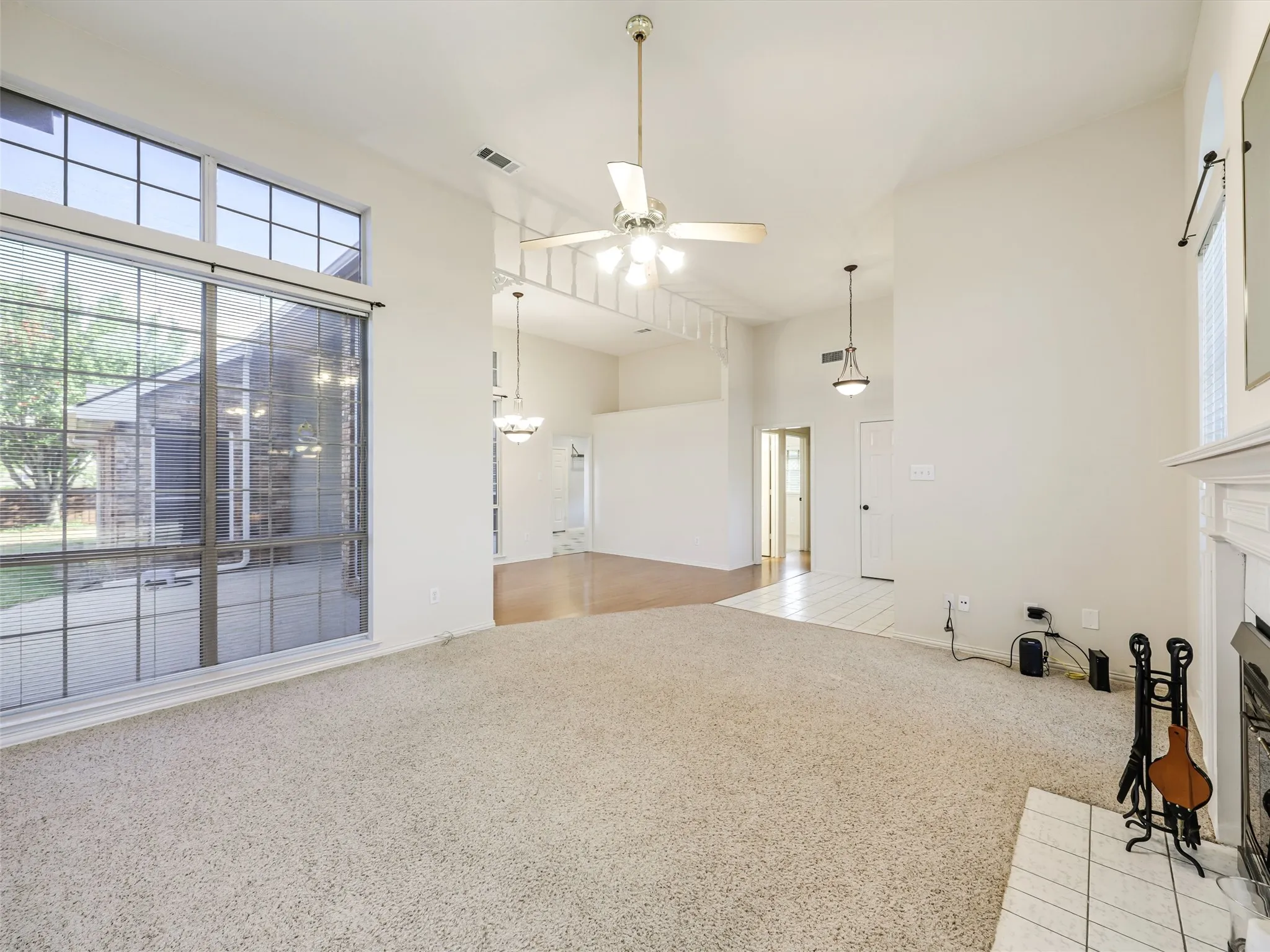 Vaulted ceilings, large picture windows, a ceiling fan, and a fireplace with a tiled hearth
