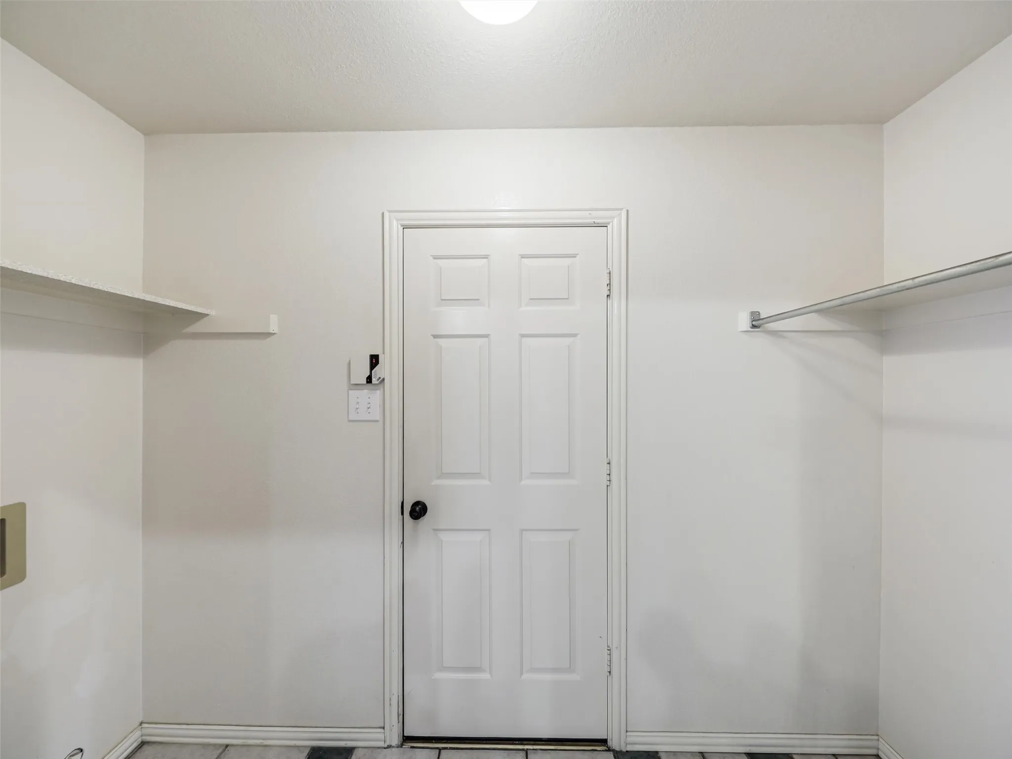 White paneled door, built-in shelving, chrome hanging rod, and tiled flooring