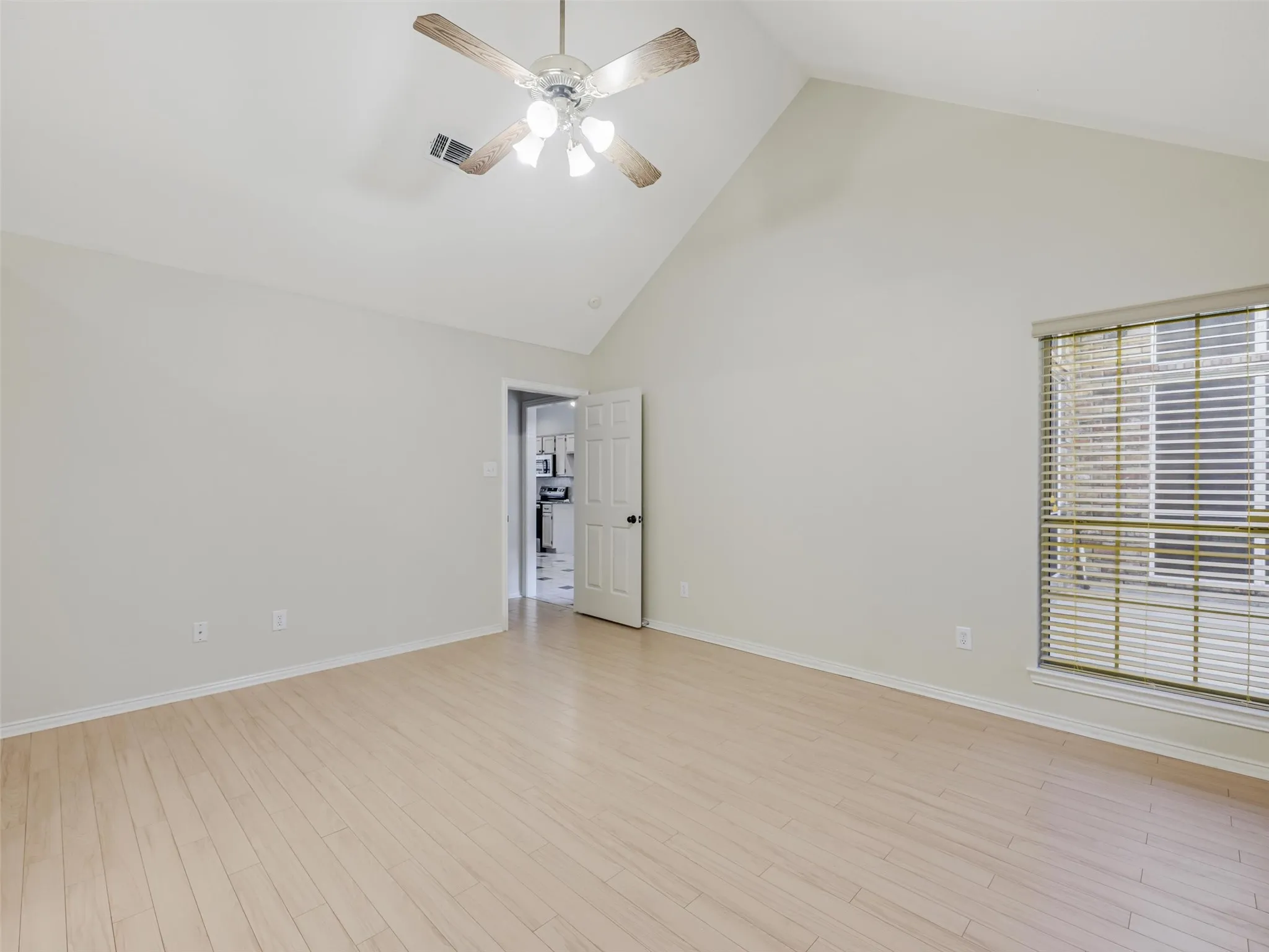 Vaulted ceiling with an attached ceiling fan, wood-finish flooring, a white paneled door, and a window with blinds