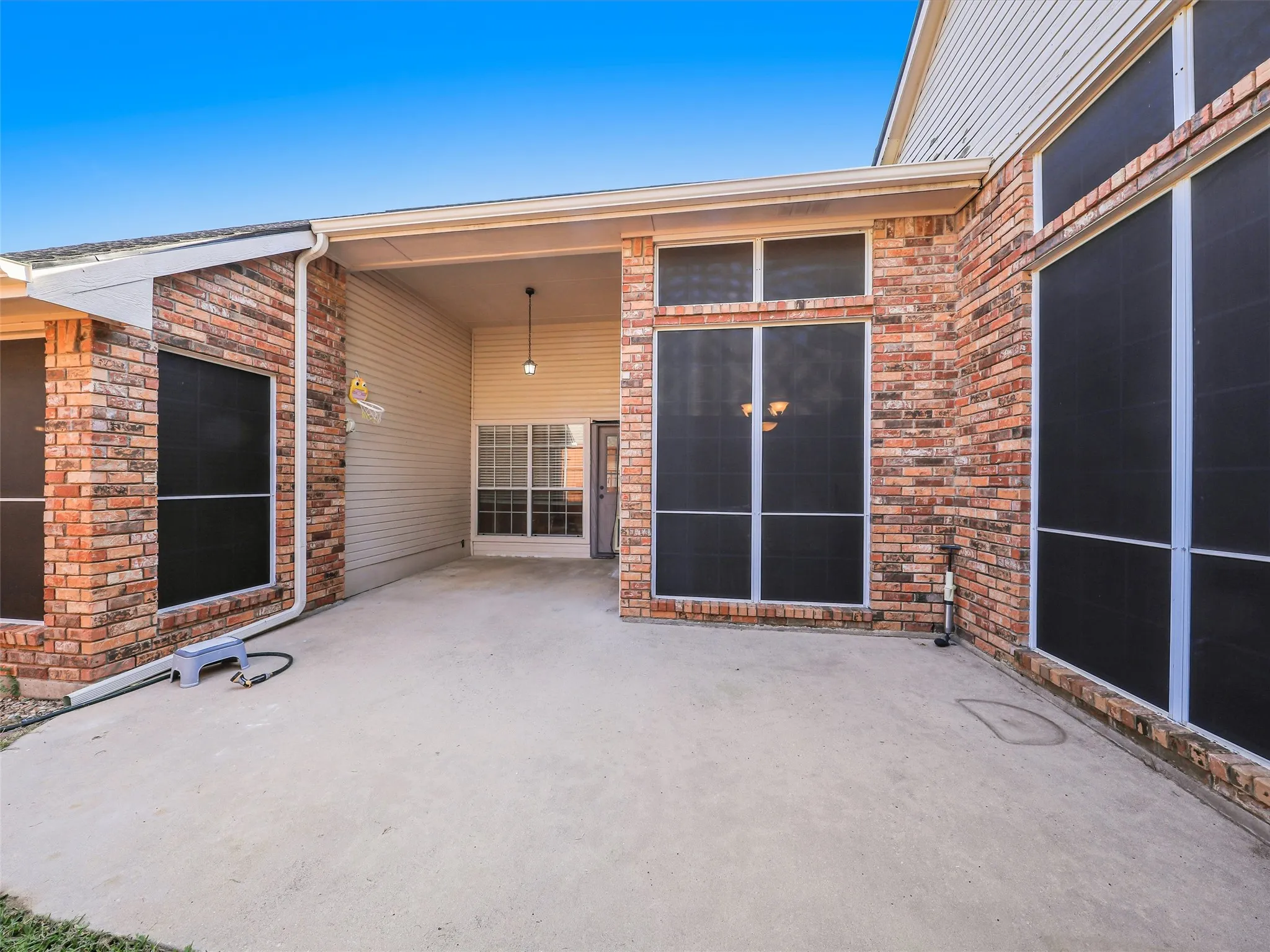 Expansive concrete patio with brick and siding exterior and large screened windows