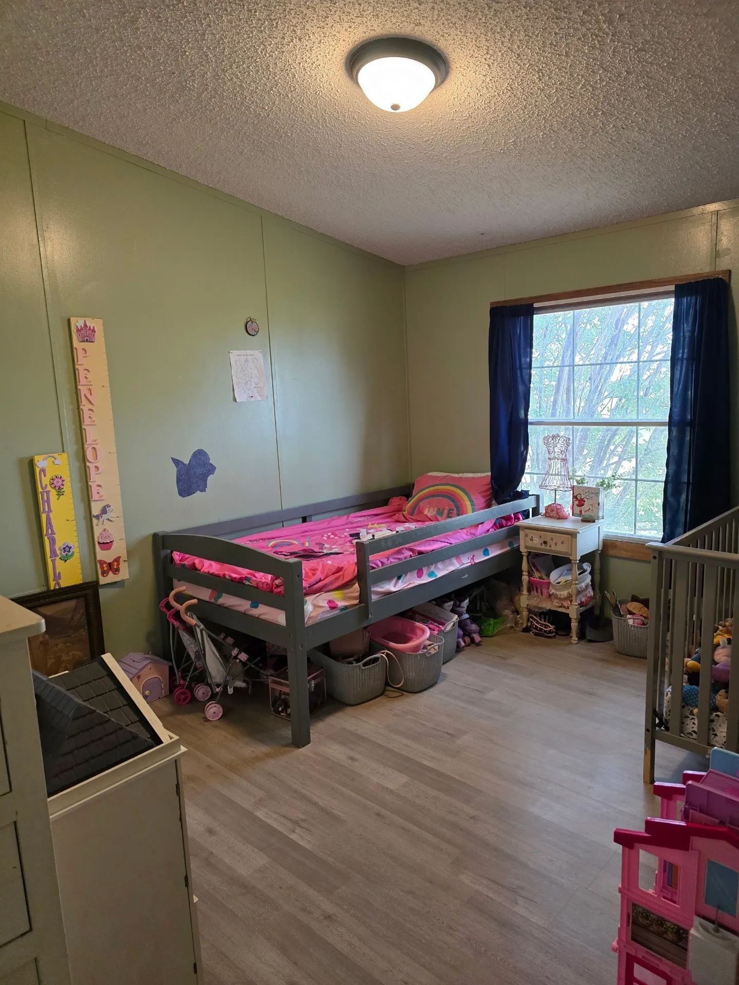 Wood-finish flooring with light green wall paneling, a large window, and a ceiling-mounted light fixture