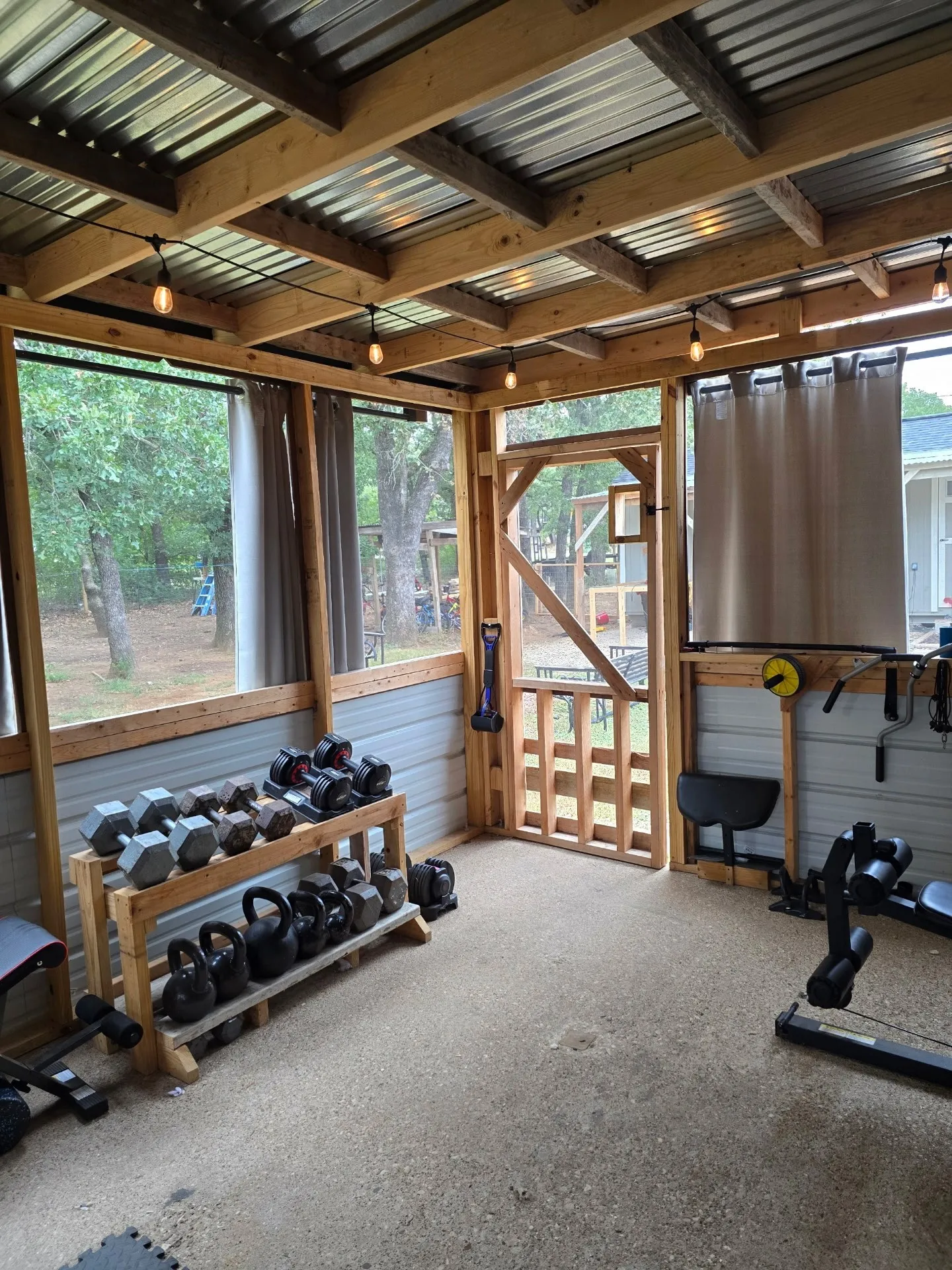 Screened room with exposed wood beam ceiling, corrugated metal roofing, and string lighting