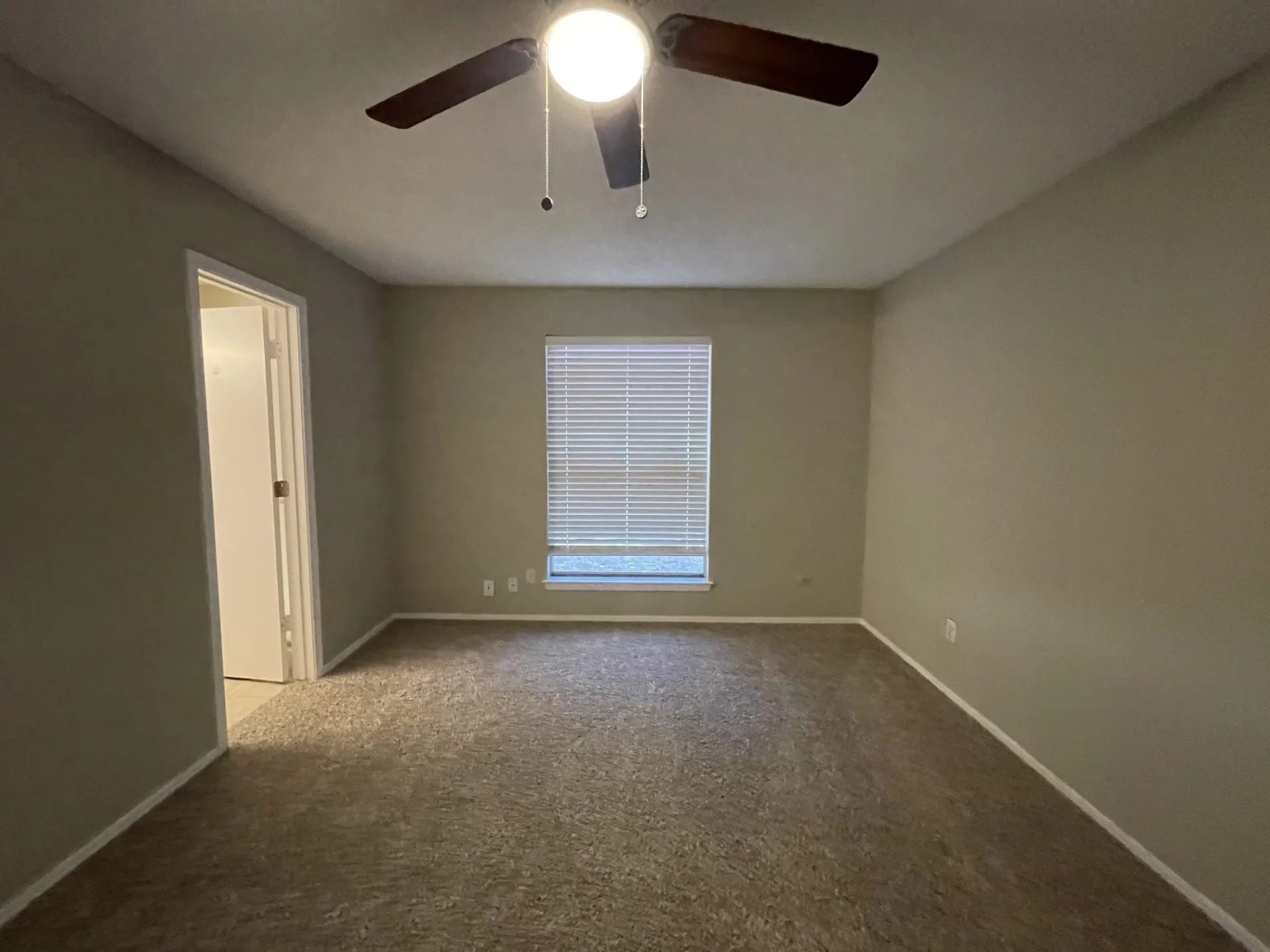 Neutral wall paint, carpeted flooring, window with blinds, ceiling fan with integrated lighting, and a white interior door