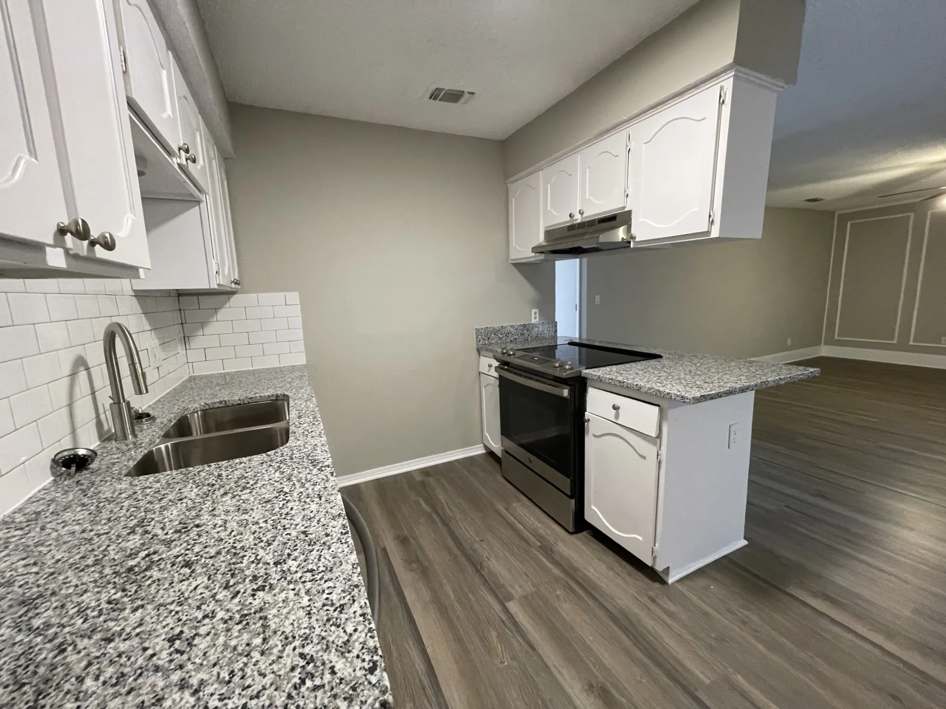 Kitchen featuring white cabinetry, granite-finish countertops, subway tile backsplash, stainless steel sink, and wood-finish flooring