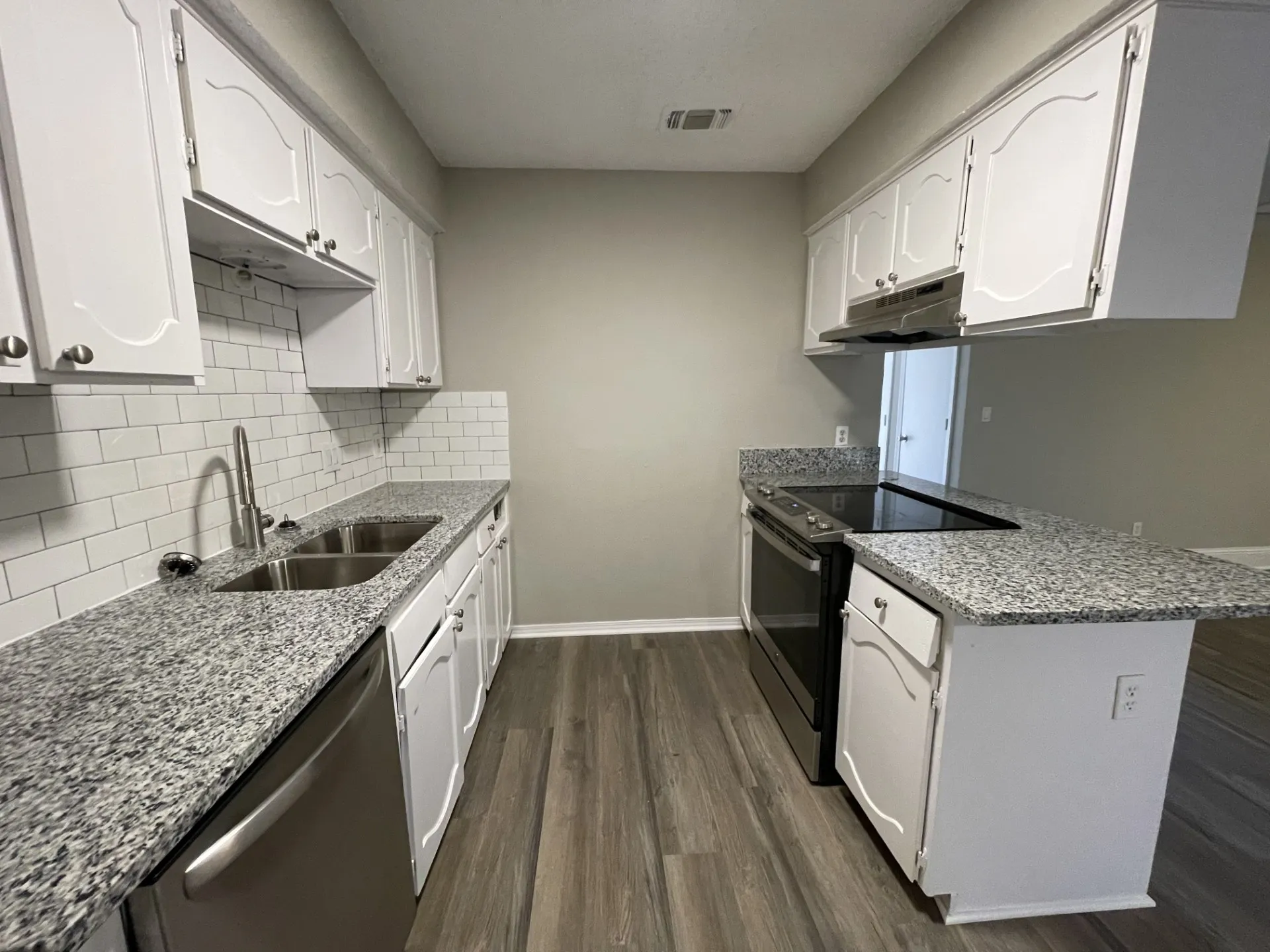Kitchen featuring white cabinetry, granite-finish countertops, stainless steel appliances, a subway tile backsplash, and wood-finish flooring