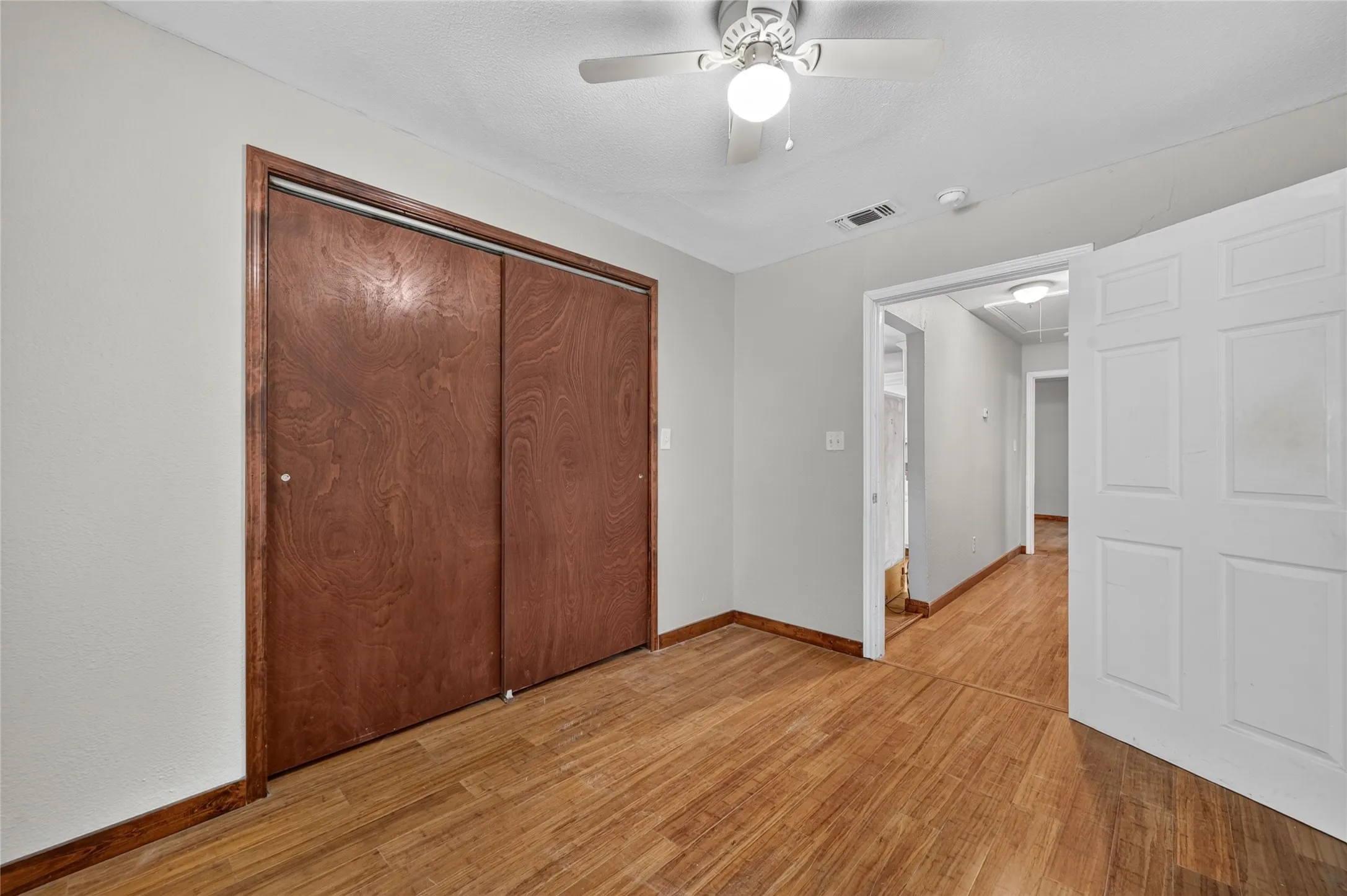 Wood-finish flooring, sliding wood closet doors, overhead ceiling fan with lighting, white interior door, and light gray wall paint
