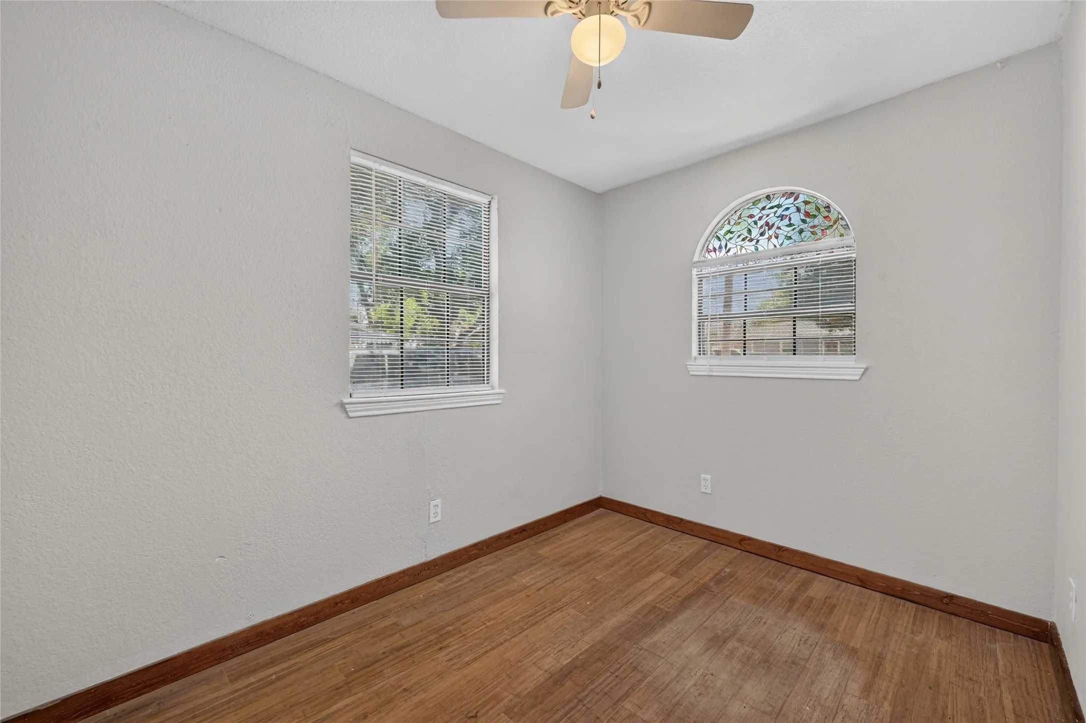 Hardwood flooring, two windows with blinds, arched window with decorative glass, and a ceiling fan with integrated lighting
