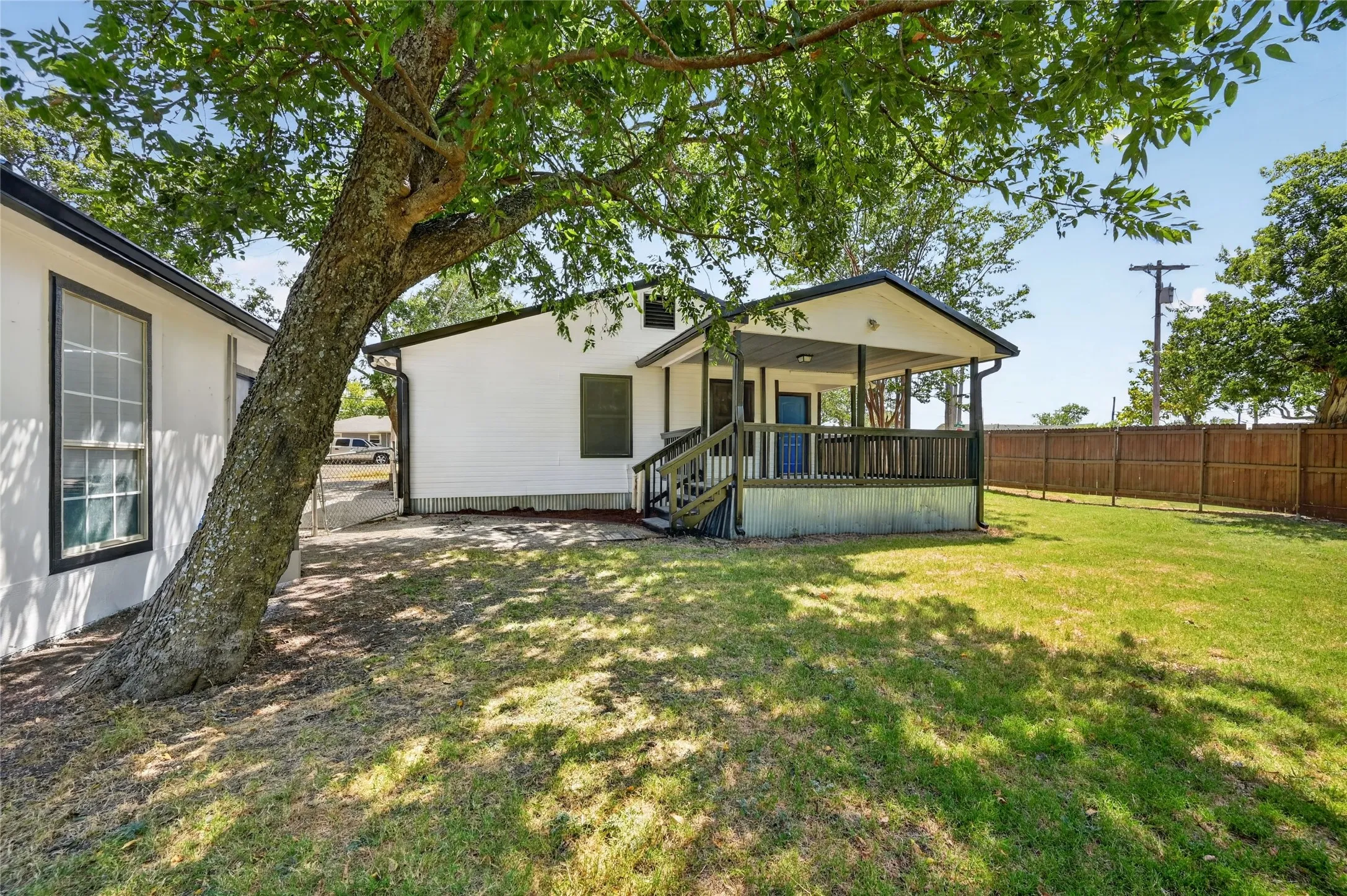 Expansive backyard with a covered porch, wood fencing, and mature trees