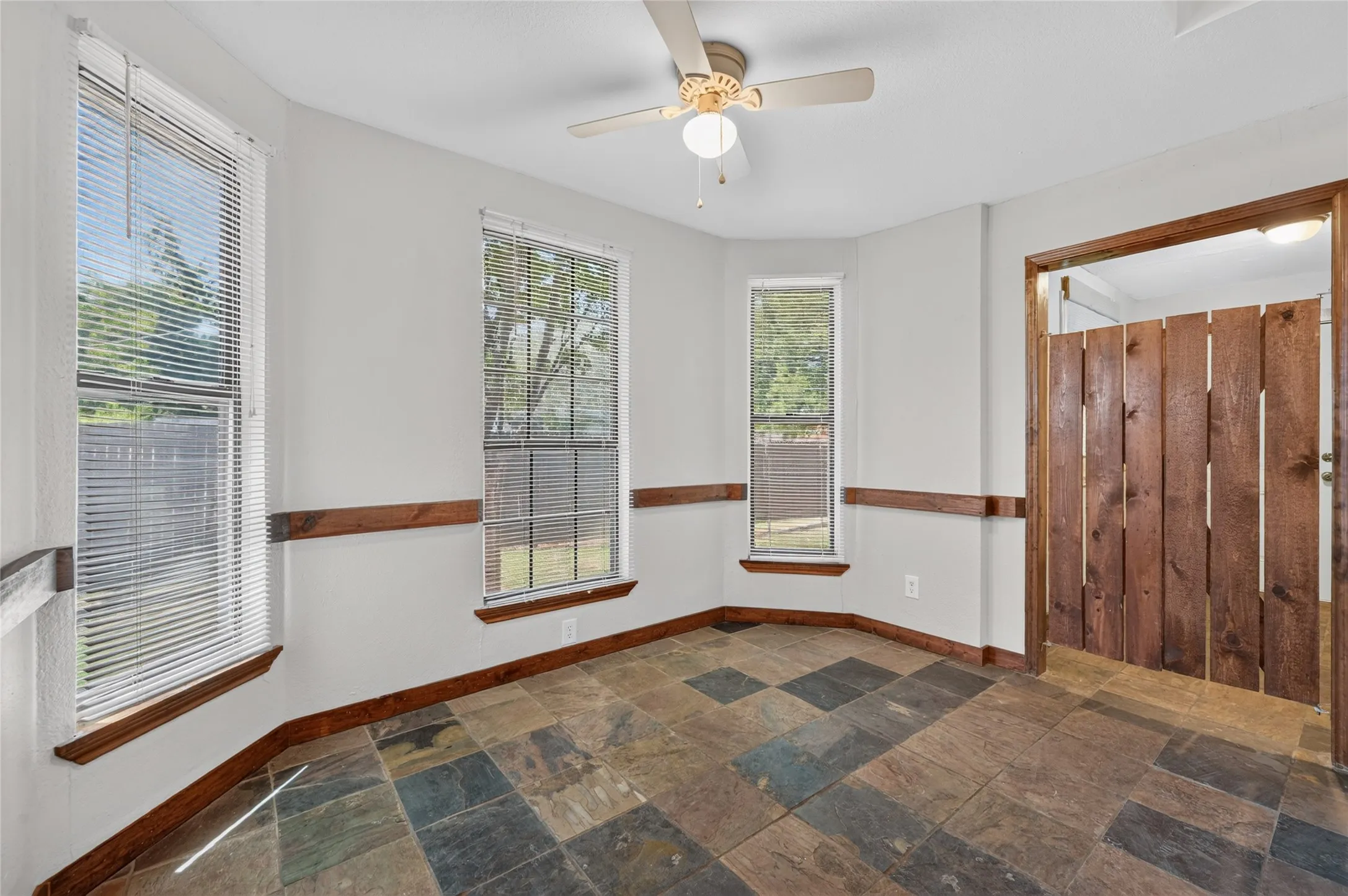 Multi-toned tile flooring, three large windows, wood trim accents, wood-paneled swinging doors, and a ceiling fan with integrated lighting