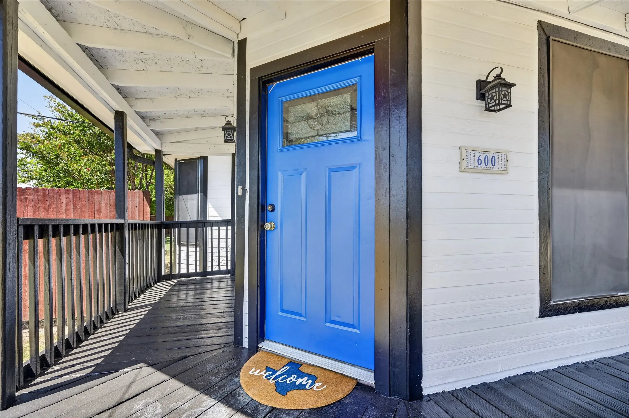 Expansive covered front porch with dark wood-finish flooring, white siding, and a blue entry door with decorative glass