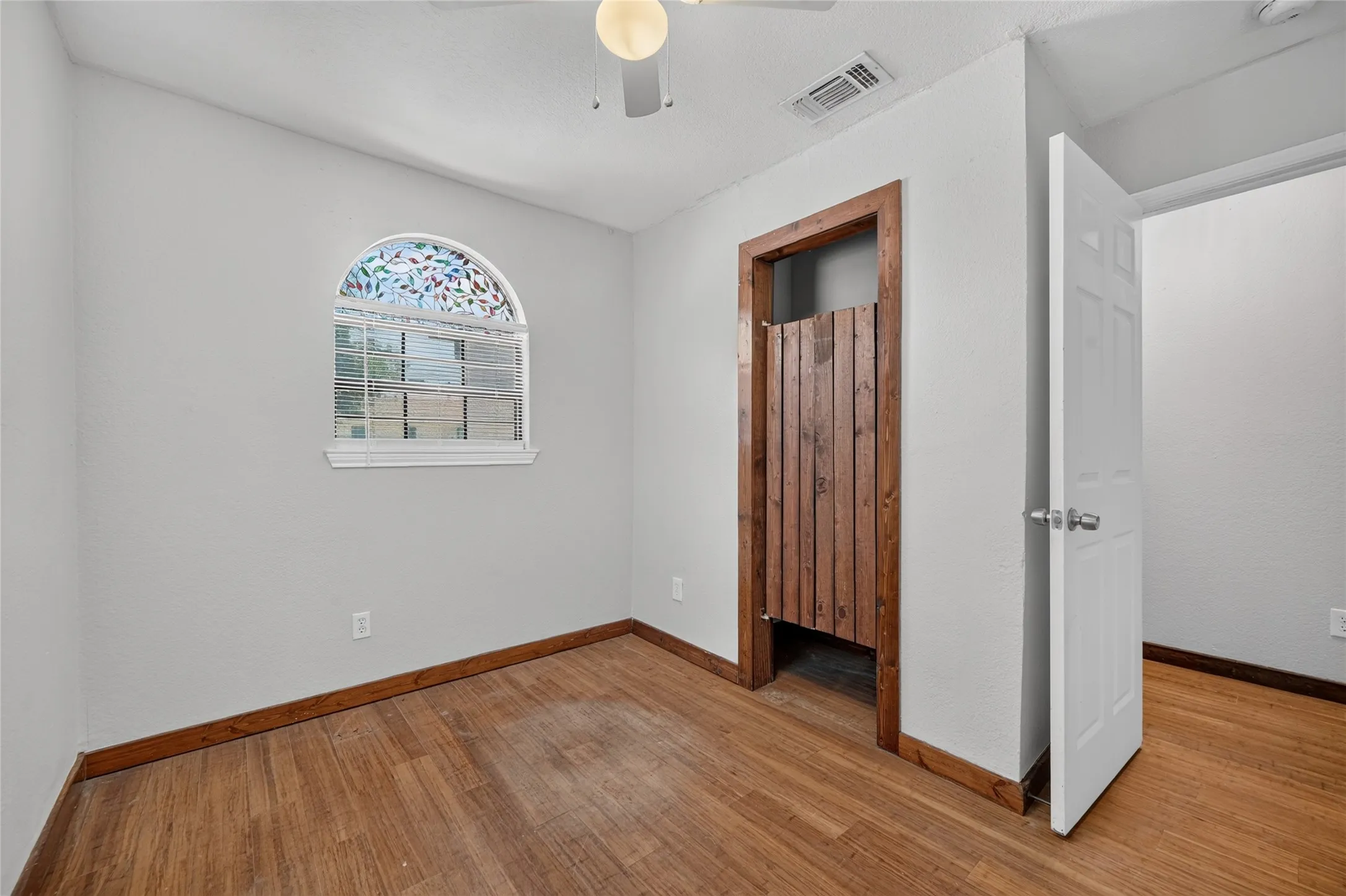 Arched window with decorative glass film, wood-finish flooring, and a ceiling-mounted light fixture