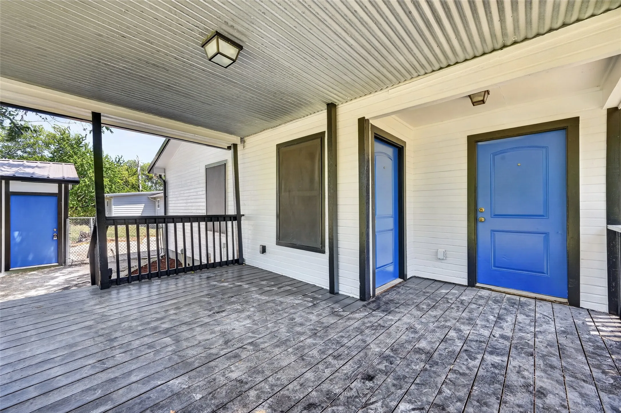 Covered porch featuring wood-finish flooring, corrugated metal ceiling, and a black railing