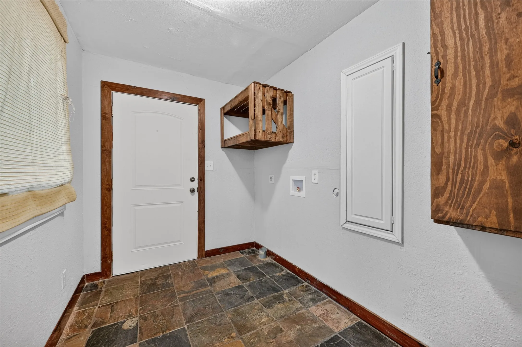 Slate-style floor tile, white door with wood-finish trim, built-in wall cabinet, and wall-mounted wood-finish shelving