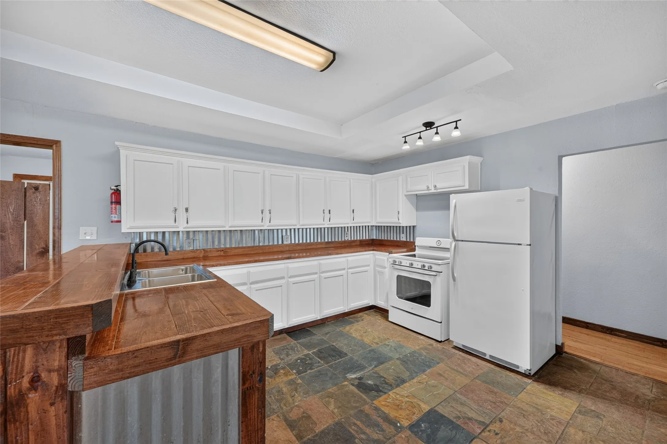 Kitchen featuring white cabinetry, slate-style floor tiling, wood-finish countertops, and a corrugated metal backsplash