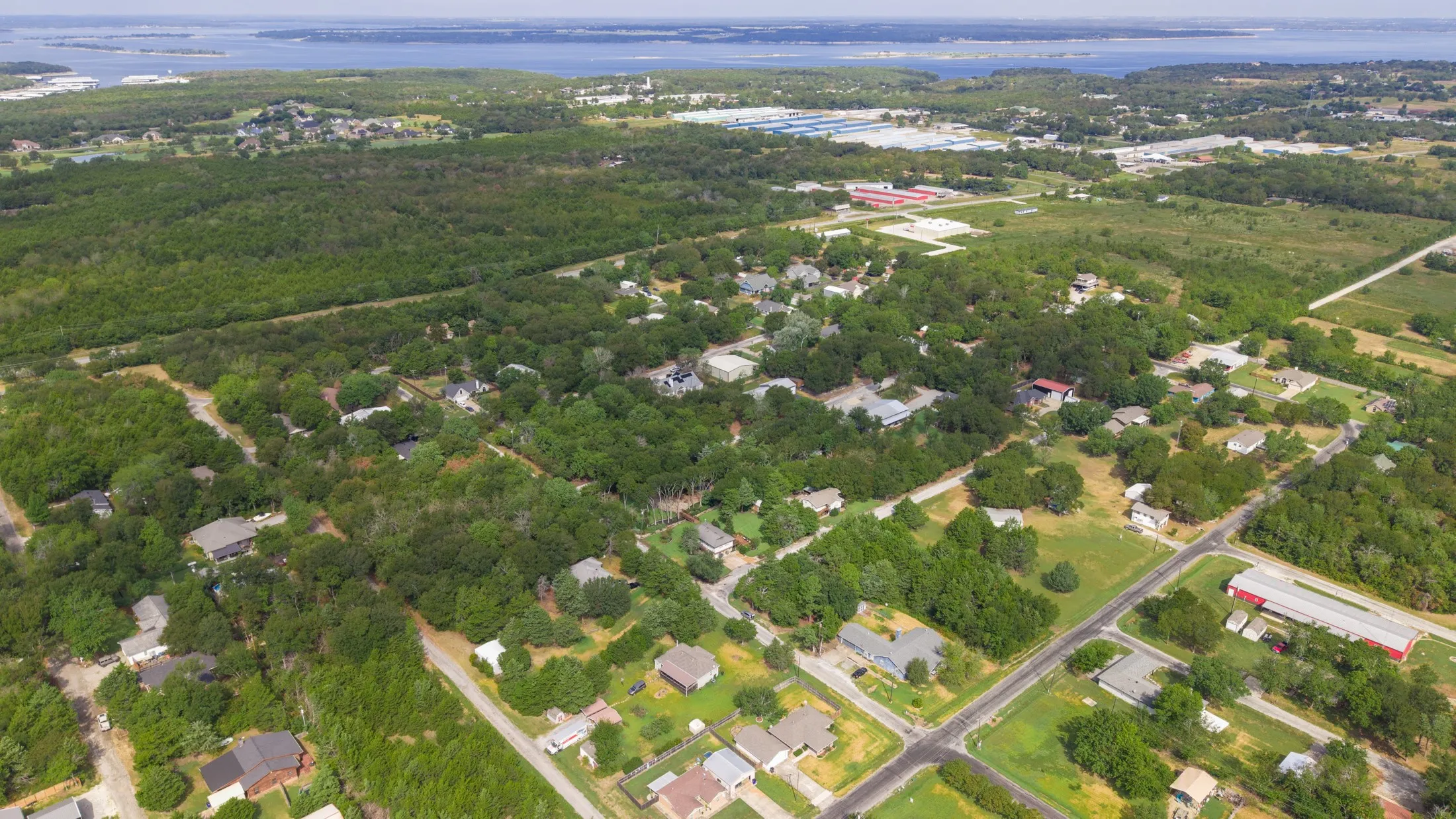 Expansive wooded areas, scattered residential dwellings, paved roadways, and distant body of water