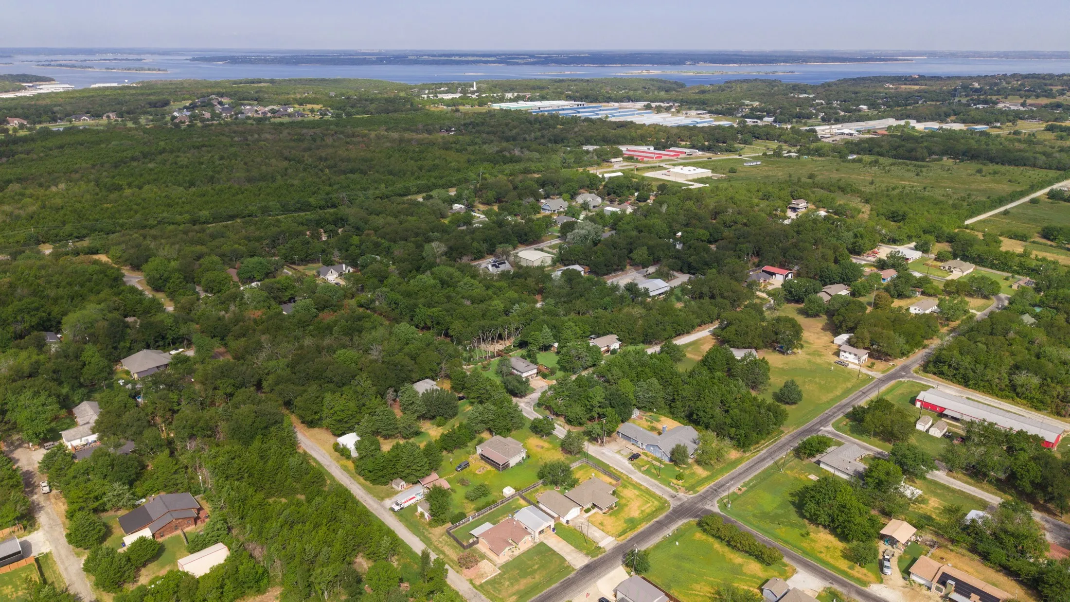 Expansive treed landscape featuring multiple residential structures and visible water body
