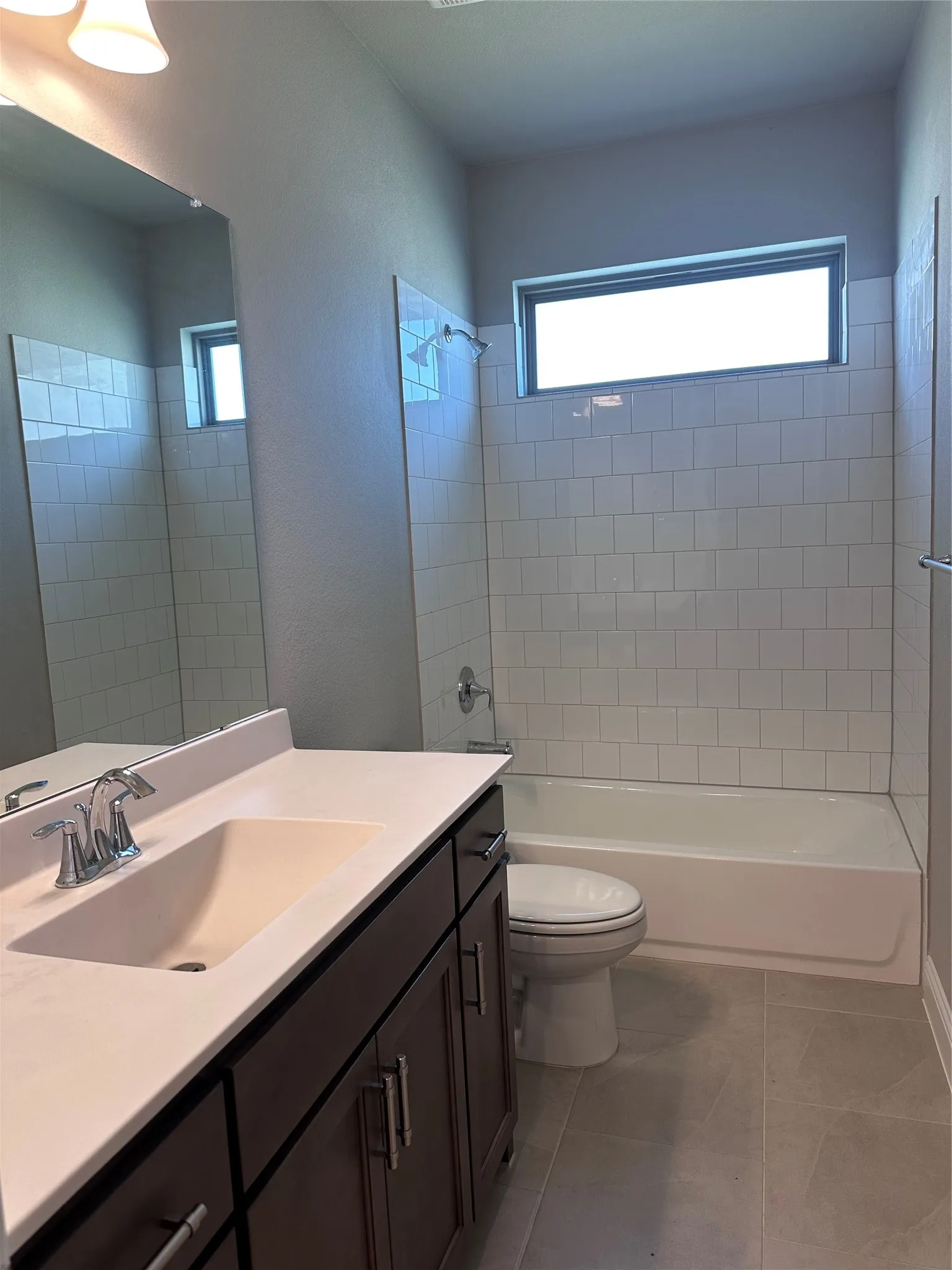 Bathroom featuring a single vanity with dark wood-finish cabinetry, a single basin sink, a bathtub with subway tile surround, and an integrated window