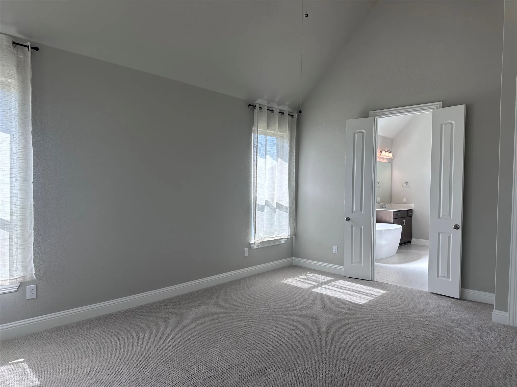 Vaulted ceiling room with dual windows, neutral wall tones, and plush carpeting