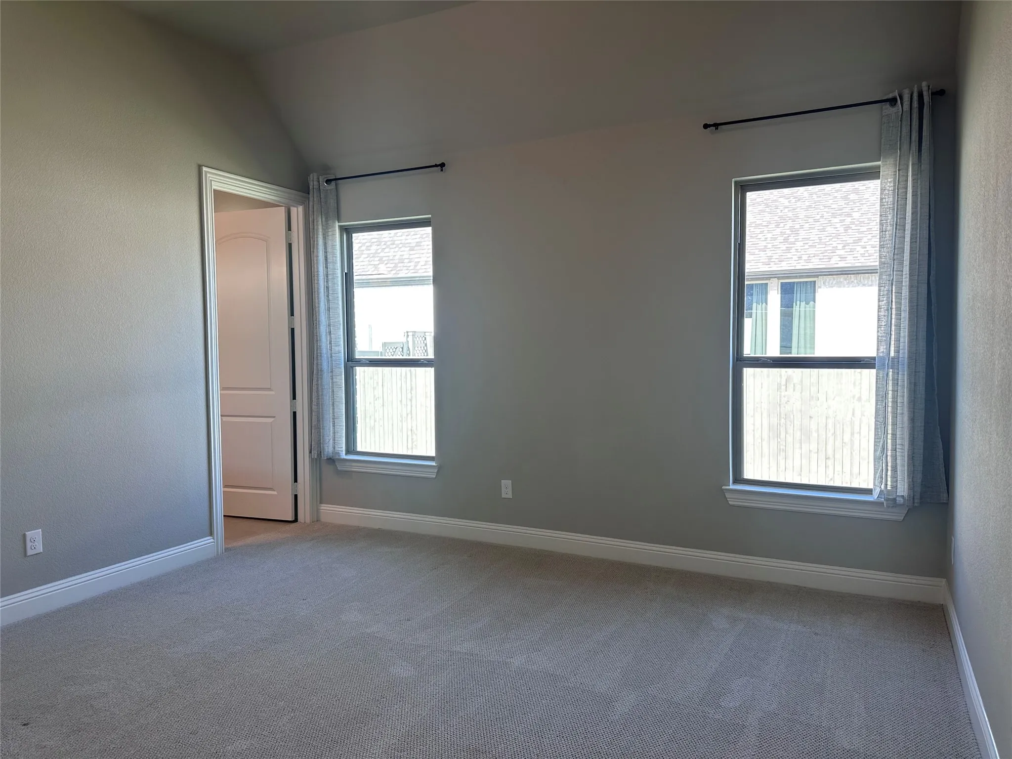 Vaulted ceiling with textured walls, two windows, wall-to-wall carpeting, and a paneled interior door