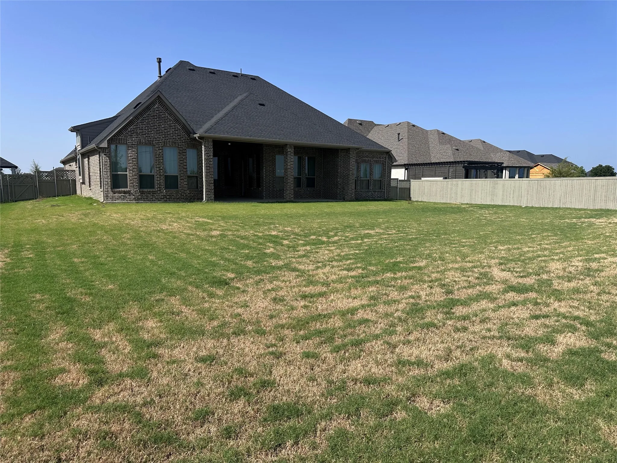 Expansive backyard featuring a privacy fence and a brick exterior with multiple windows
