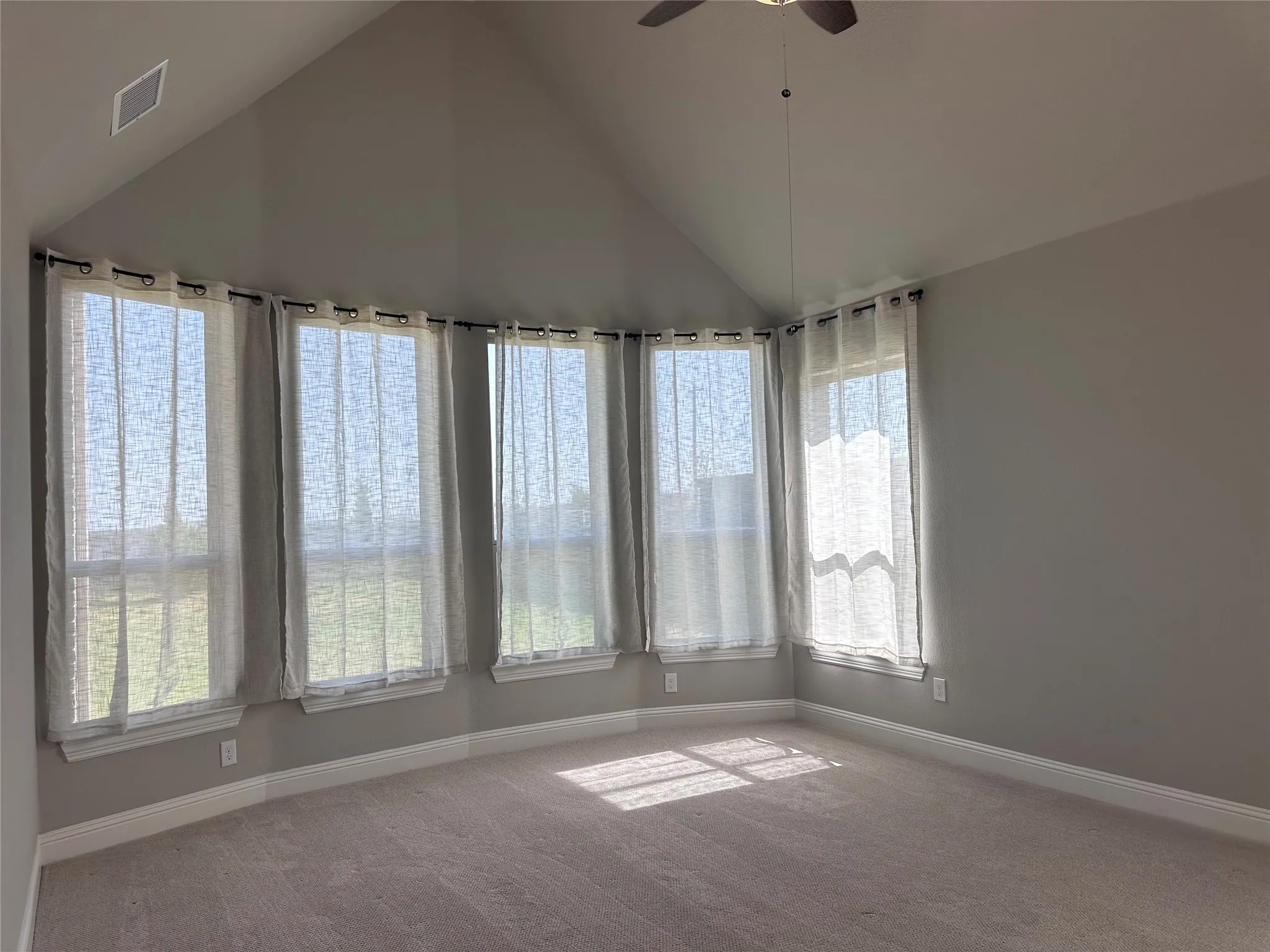Vaulted ceiling room featuring a ceiling fan, five large windows, and neutral carpeting