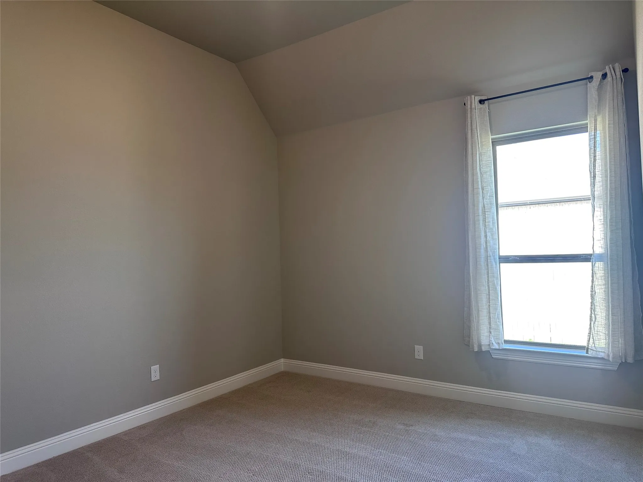 Neutral paint palette with sloped ceiling, carpeted flooring, and a window with white trim