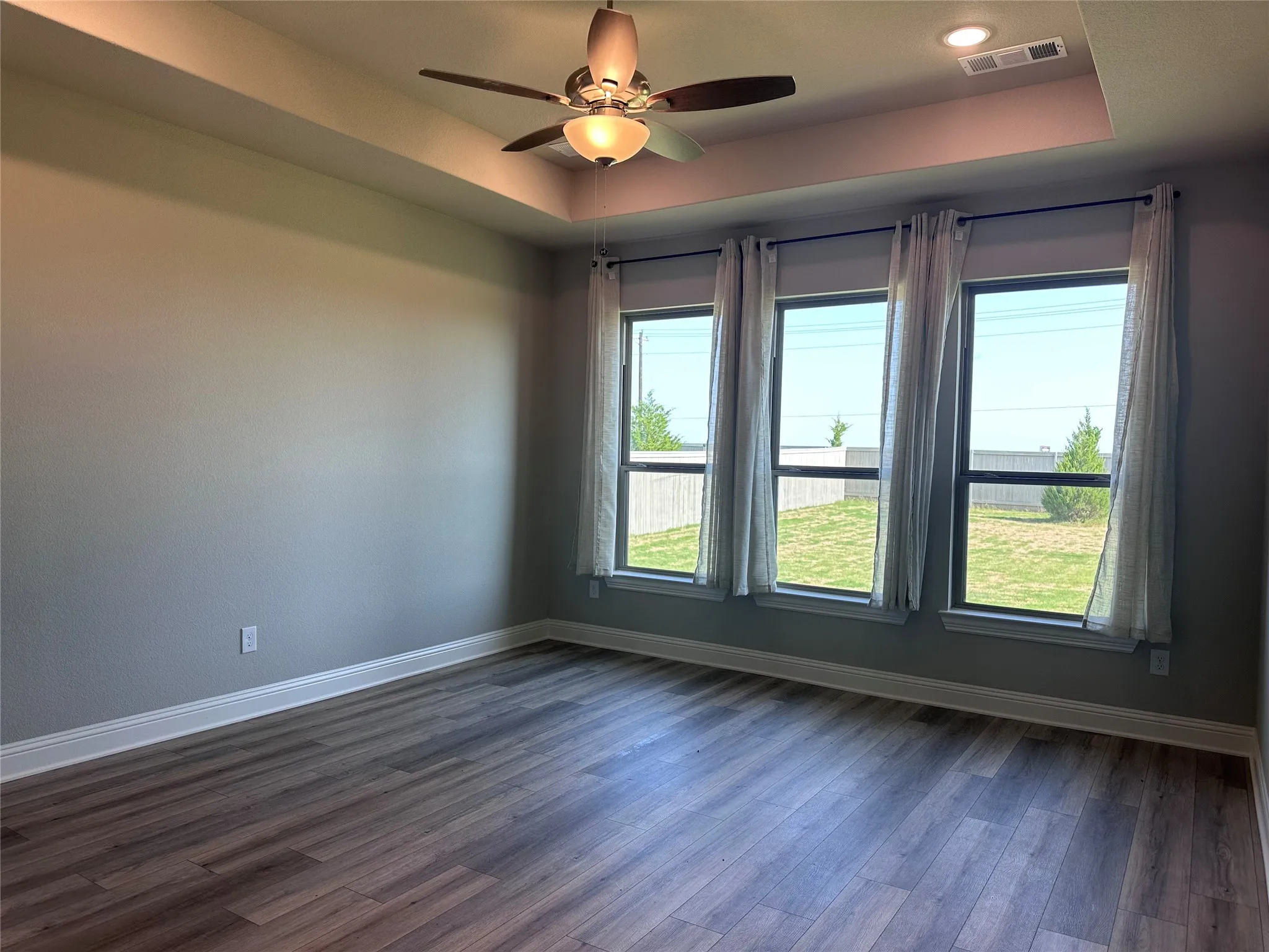Tray ceiling with recessed lighting, ceiling fan with integrated light, wood-finish flooring, and multiple windows