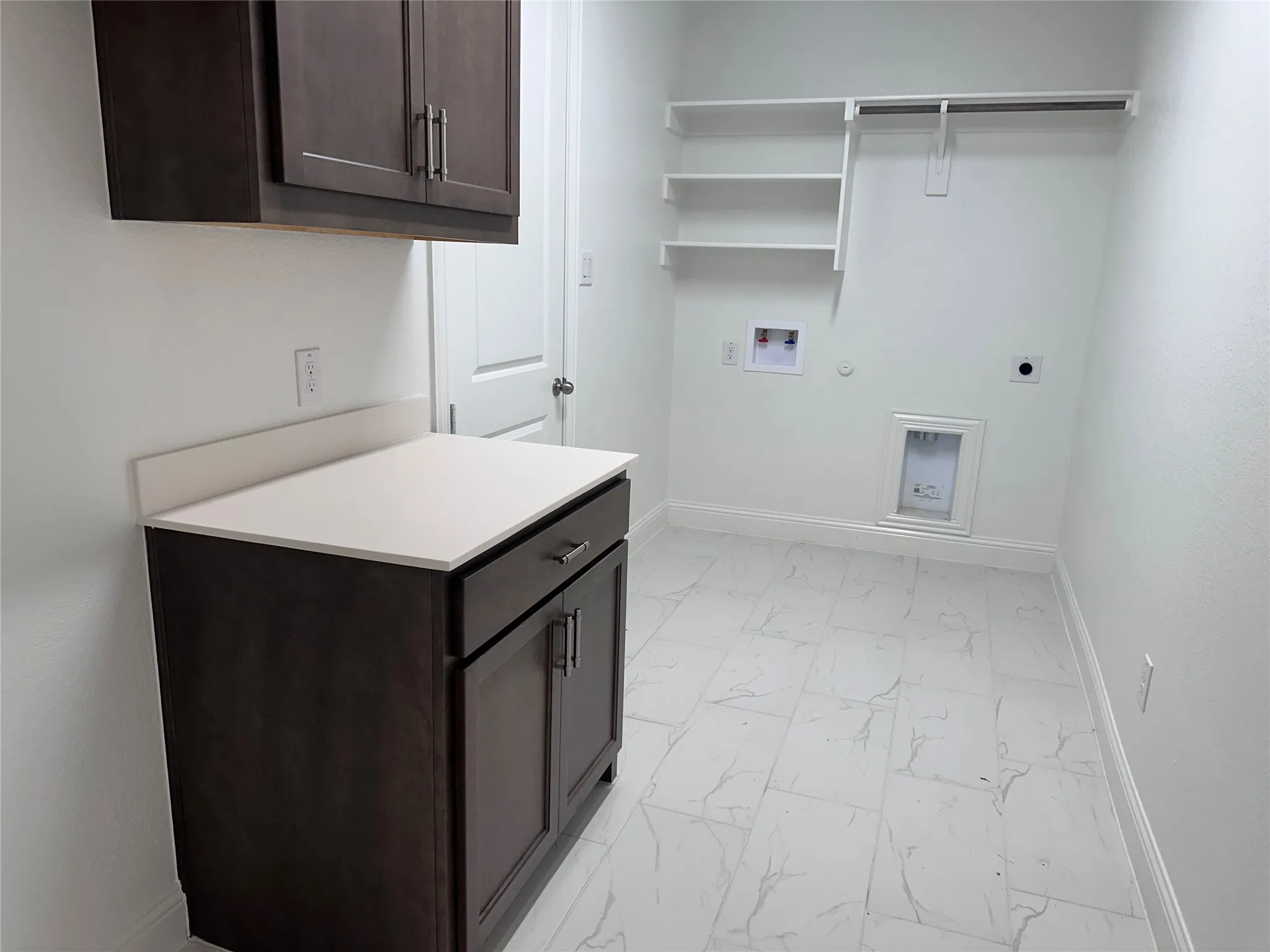 White tile flooring, dark wood-finish cabinetry, light-toned countertop, wall-mounted shelving, and a garment rod