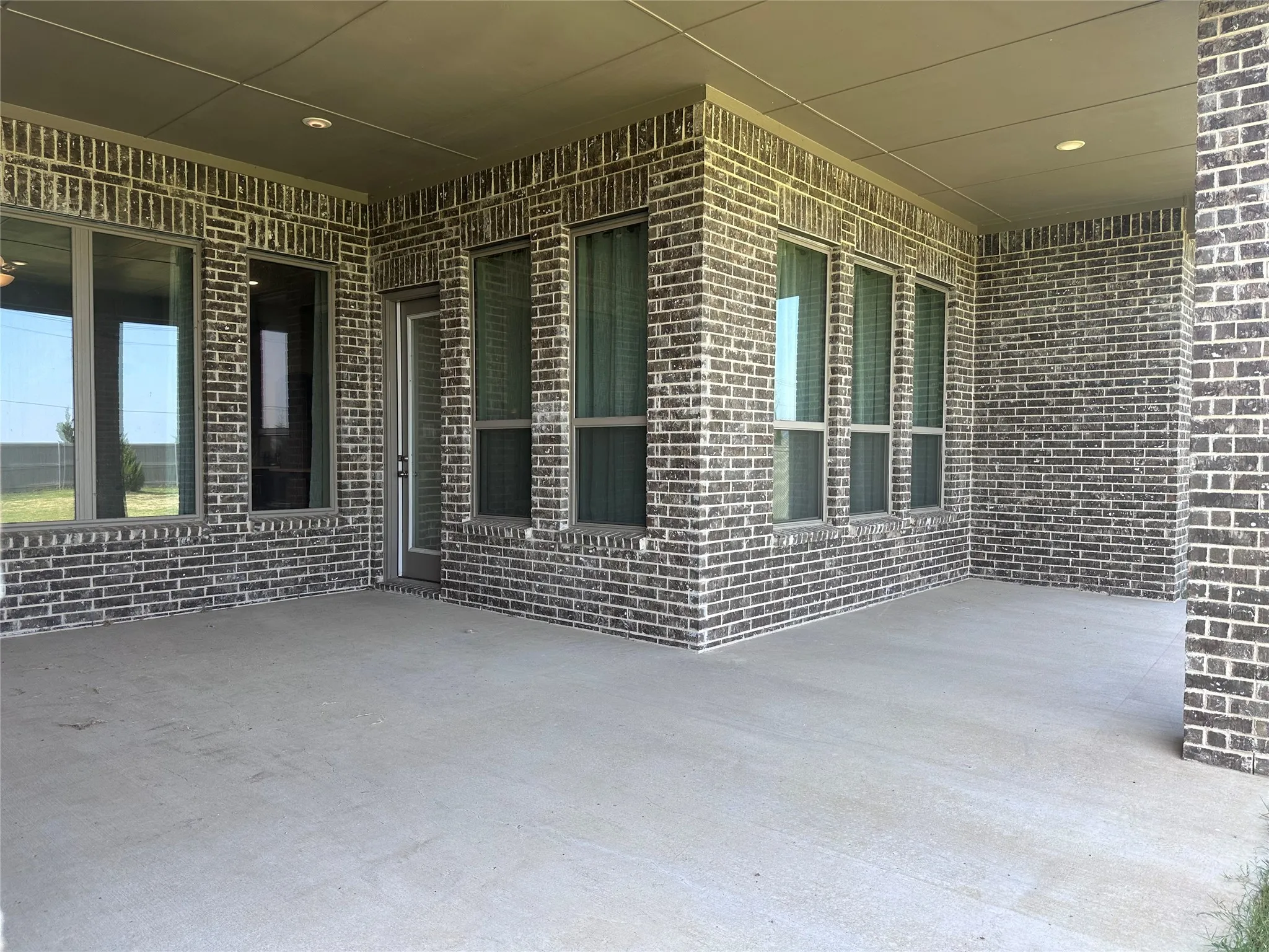 Covered patio with a concrete surface, brick exterior, multiple windows, and recessed lighting