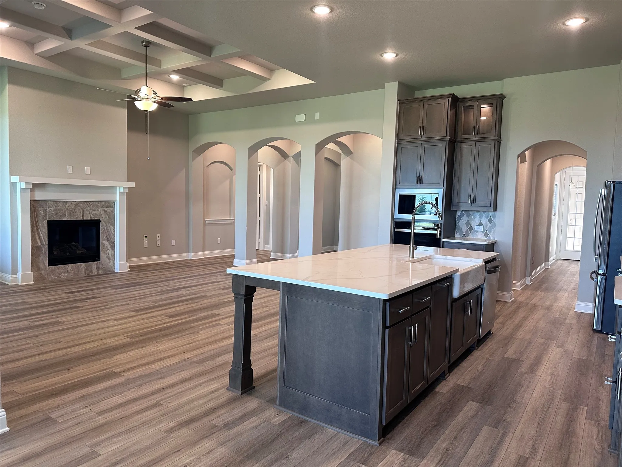 Open-concept living area with wood-finish flooring, a coffered ceiling, and a fireplace with a stone surround