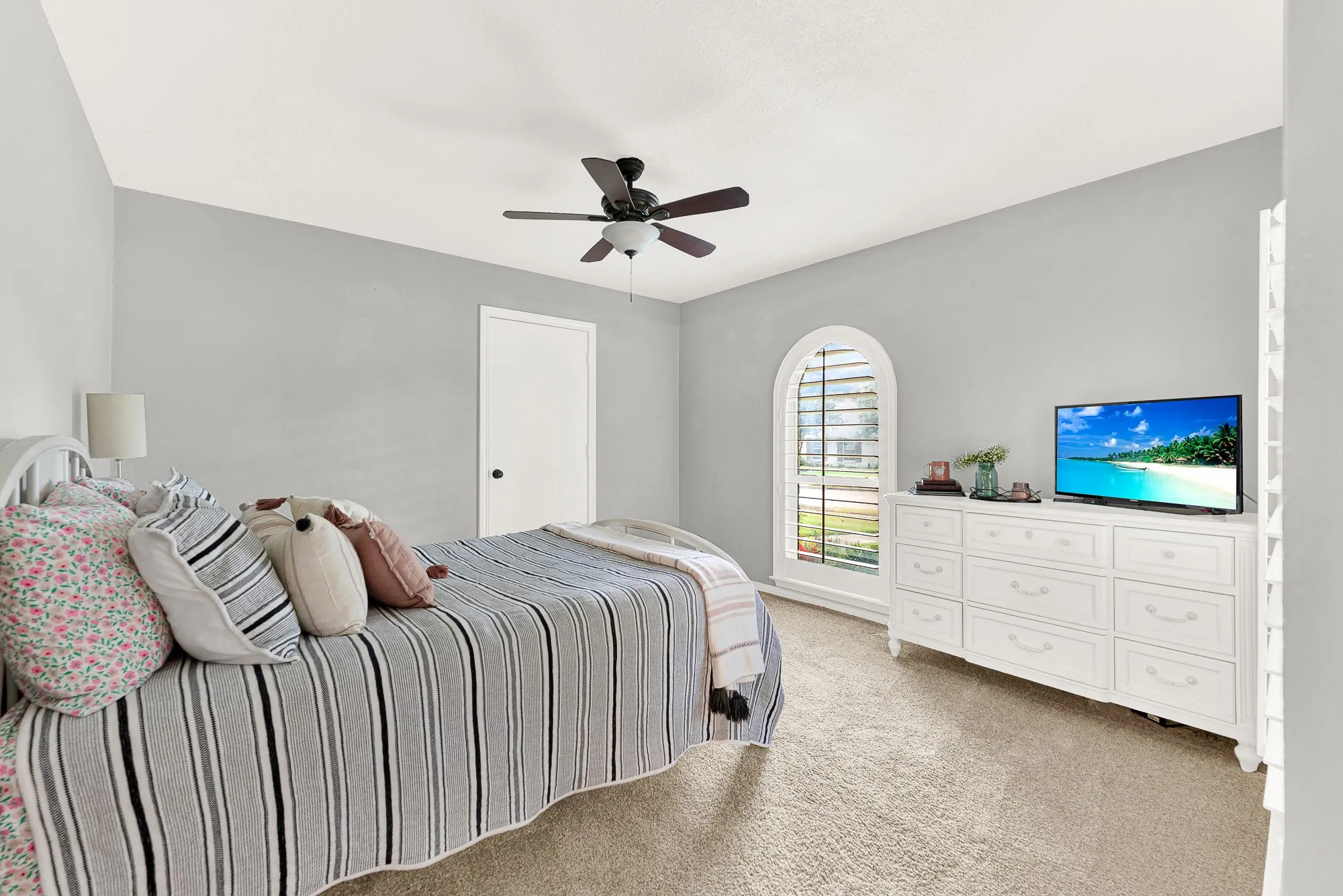An elegant arched cottage window serves as a striking focal point in this additional bedroom. High ceilings, soft gray walls, and plush carpet make the room feel spacious and inviting