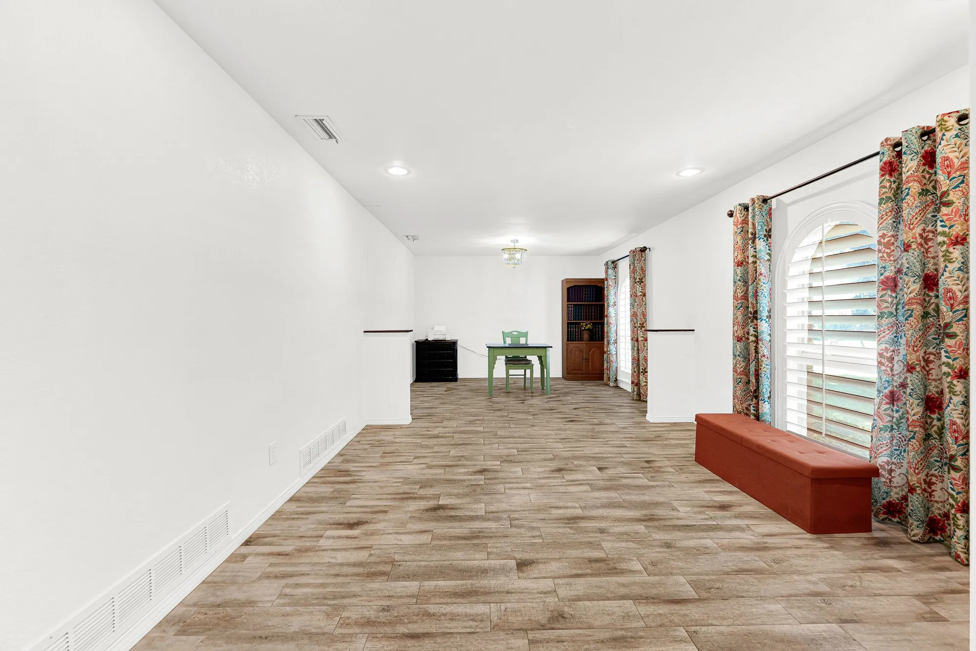 Stretching along the front of the home, an expansive multi-use space offers endless layout possibilities for modern living. Arched windows dressed in vibrant drapery fill the room with gentle daylight, creating an inspiring environment for a home office, media lounge, or play are