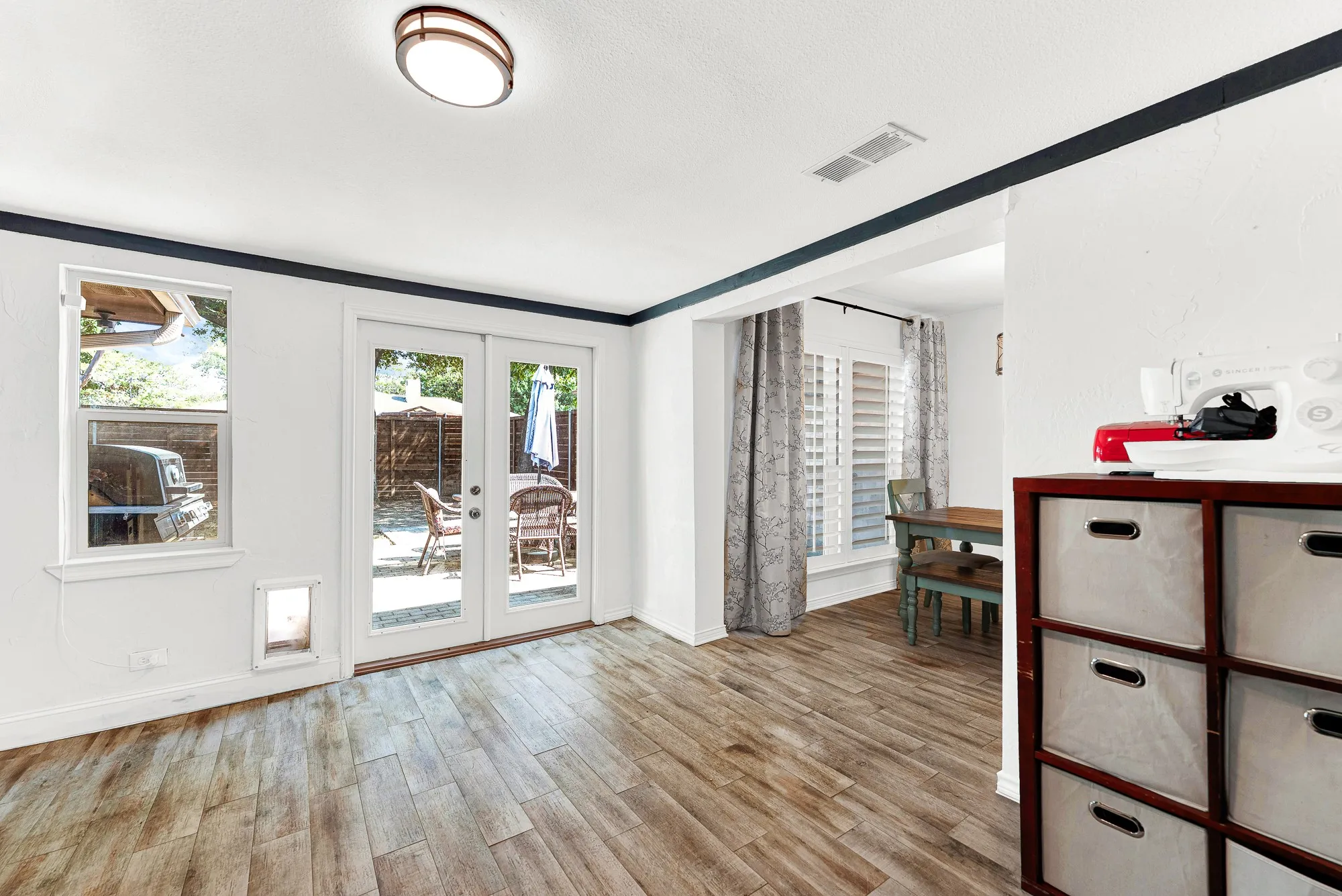 French doors open directly out to the back patio, flooding the space with natural light and fresh outdoor views. The wide open transition into the dining area keeps household routines connected and fluid