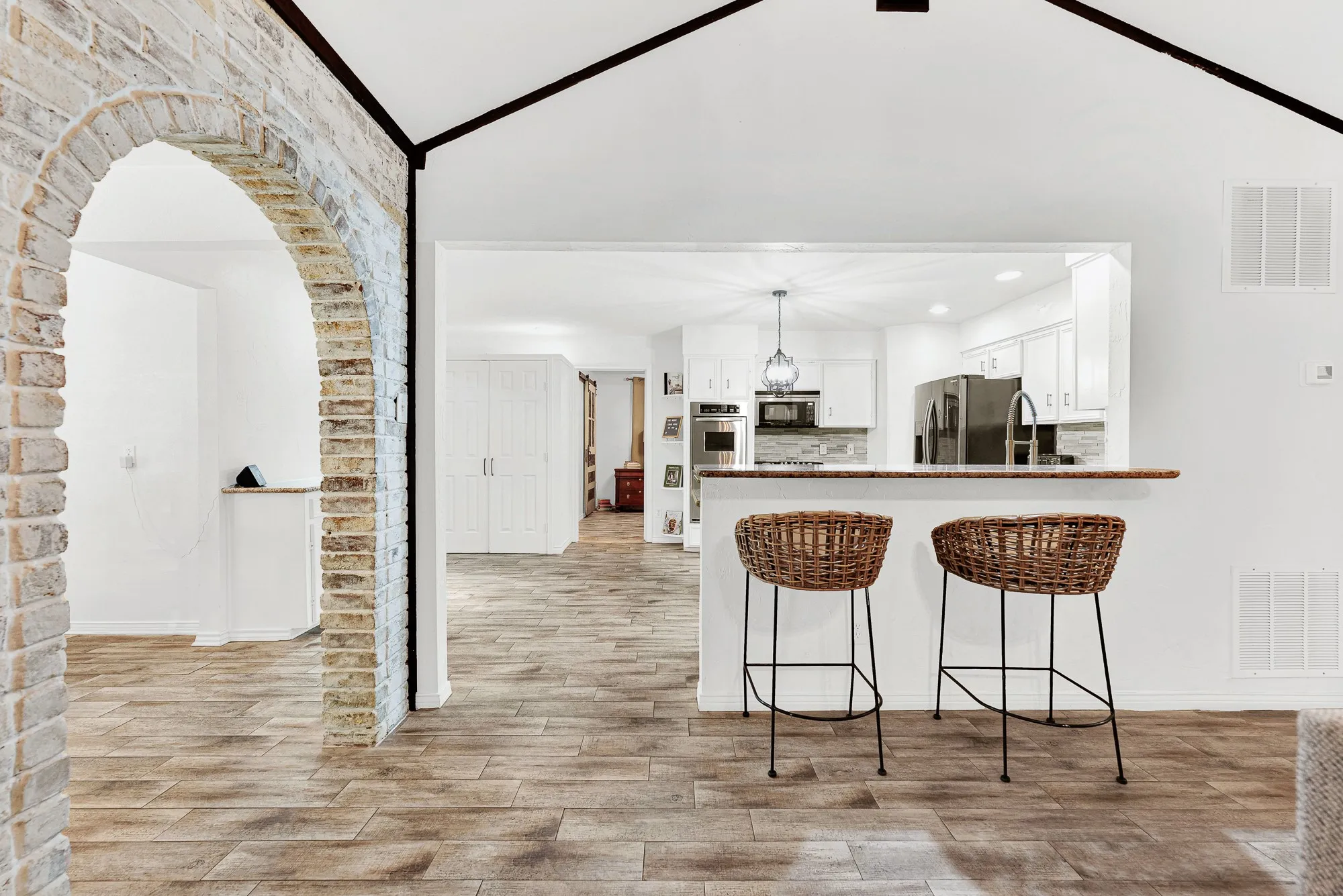 Framed by a character-rich brick archway, this view showcases the raised breakfast bar and open sightlines into the updated kitchen. It is the perfect spot for friends to pull up a stool and chat while you prep drinks or evening appetize