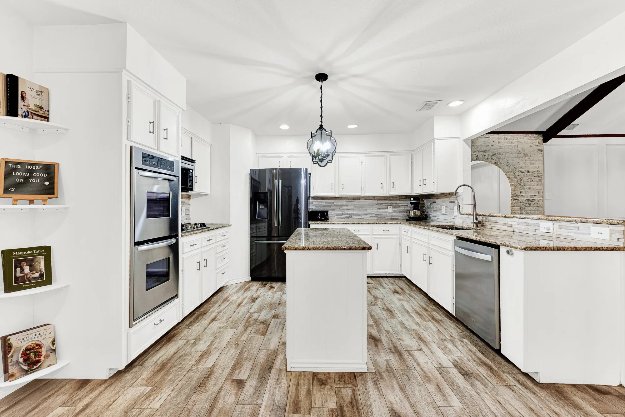 A straight-on view captures the granite center island, crisp white cabinetry, stainless appliances, and stylish stone backsplash. Cooking family meals becomes an absolute joy with abundant counter space and double wall ovens ready for any holiday feast.
