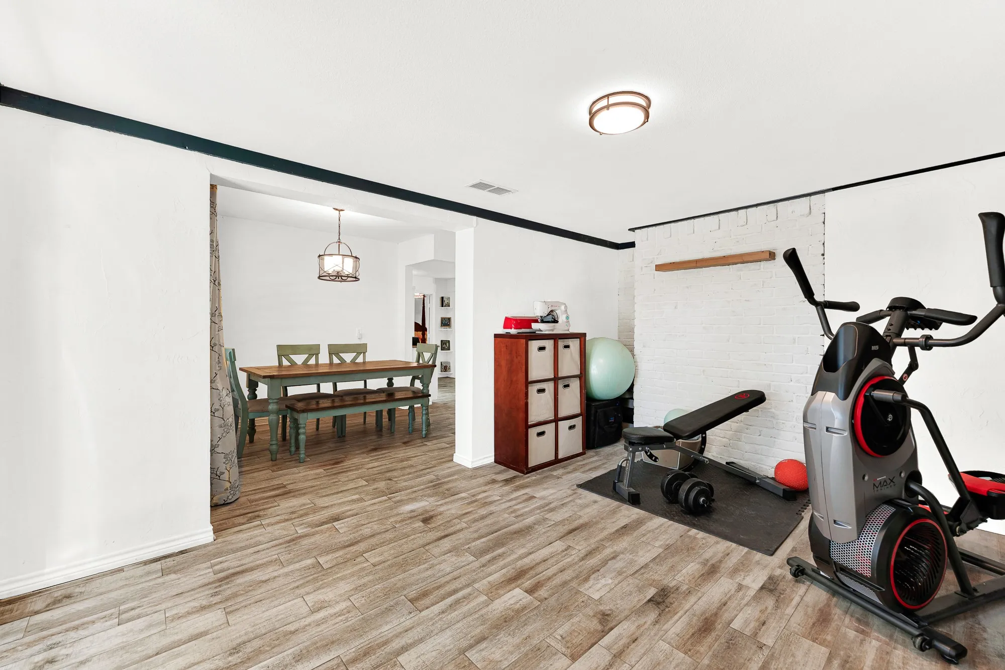 Continuous wood-look tile flooring flows seamlessly between the dining area and this versatile bonus space. High ceilings and clean sightlines create an inviting layout ready for fitness gear, crafting setups, or extra seating