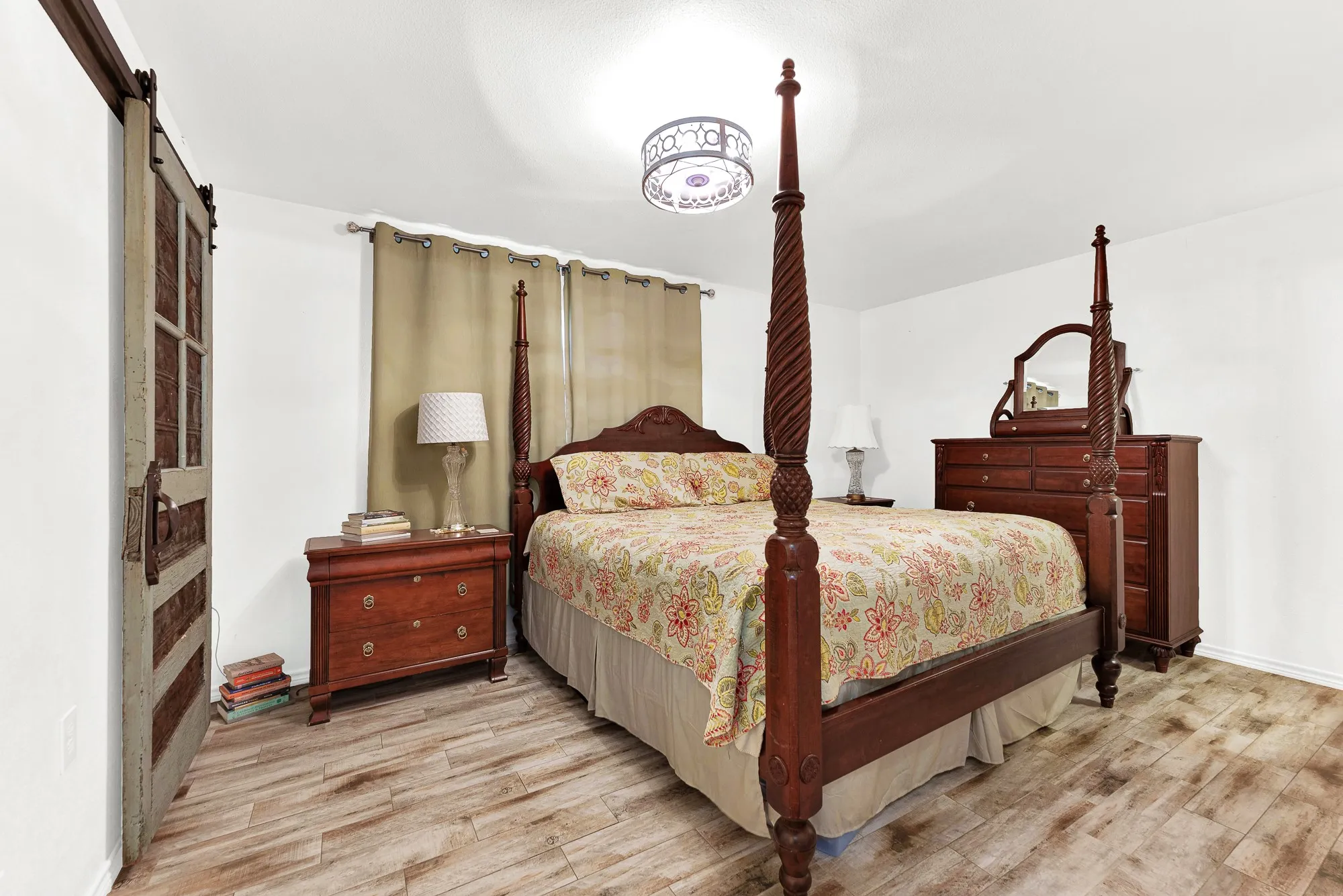 Rich wood finishes, a stately four-poster bed, and unique sliding barn doors anchor this restful primary suite. Plenty of space for matching dressers and nightstands creates a balanced, peaceful retreat to recharge at the end of the day.