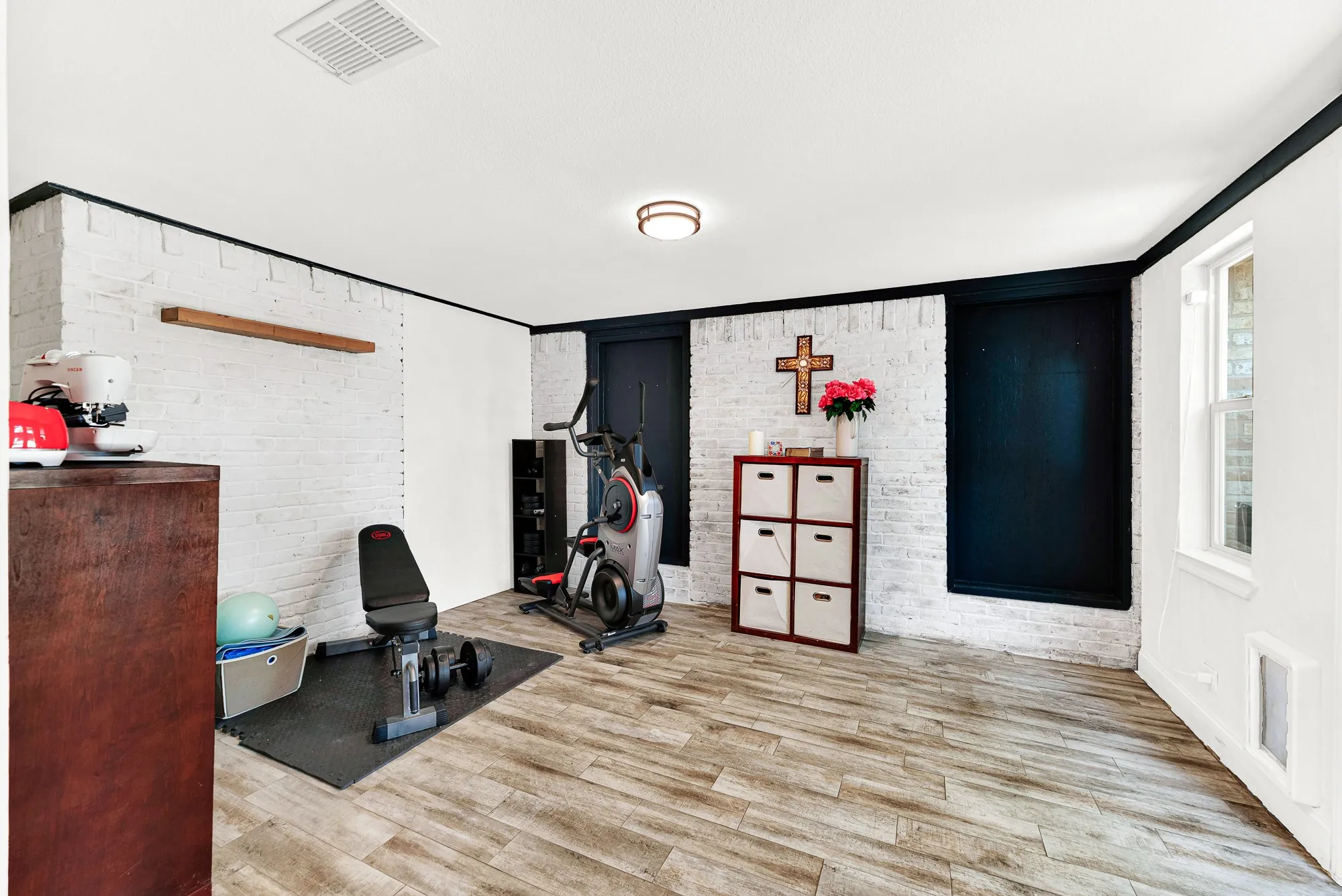 Painted brick accents and crisp black trim give this flexible room off the dining area distinct character and warmth. Generous floor space makes it simple to configure a private home gym, hobby station, or secondary lounge.