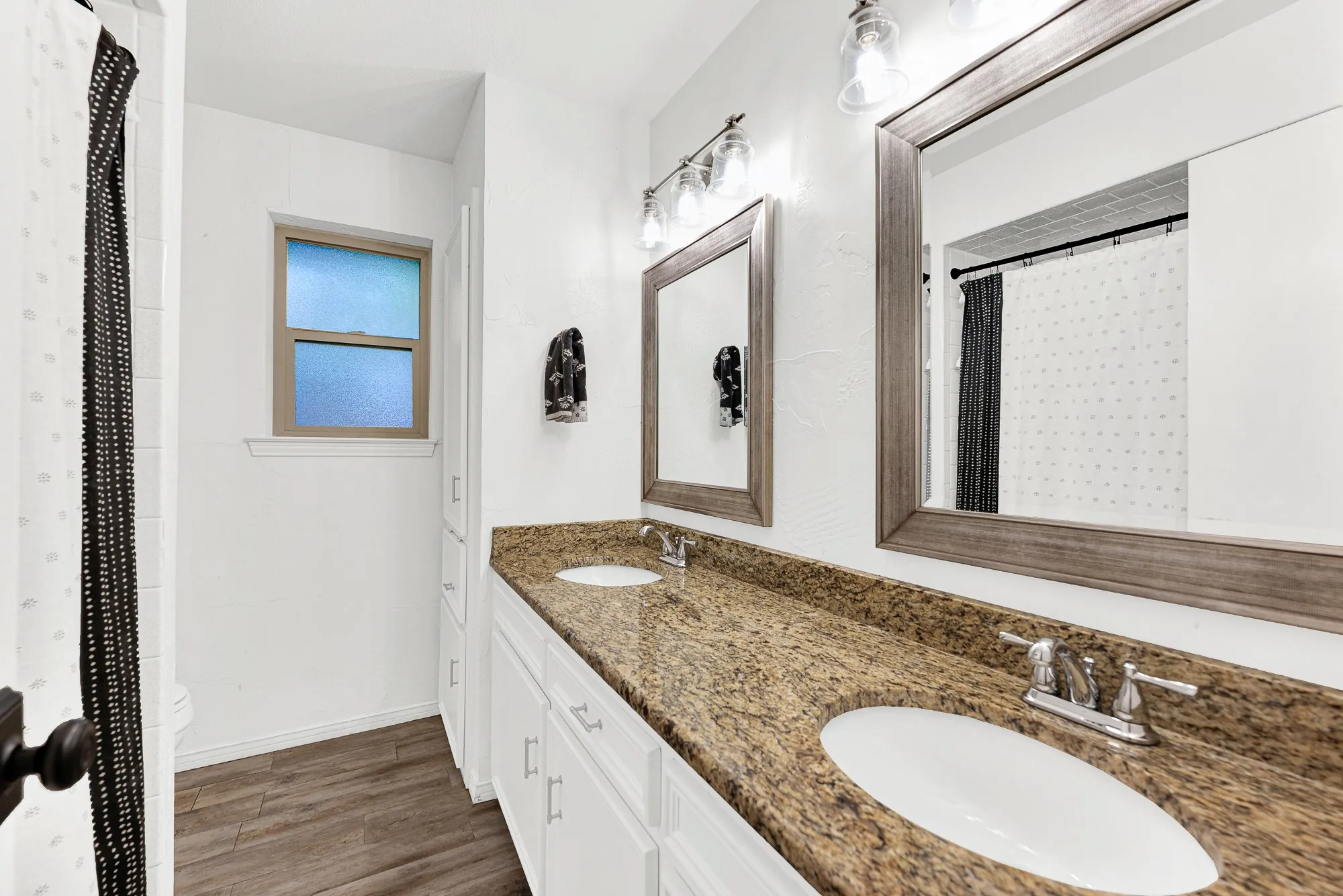 Serving the secondary bedrooms, this expansive shared full bath features an extended double-sink granite vanity with ample lower drawers and twin framed mirrors. Built-in linen storage and a privacy window complete the functional design.
