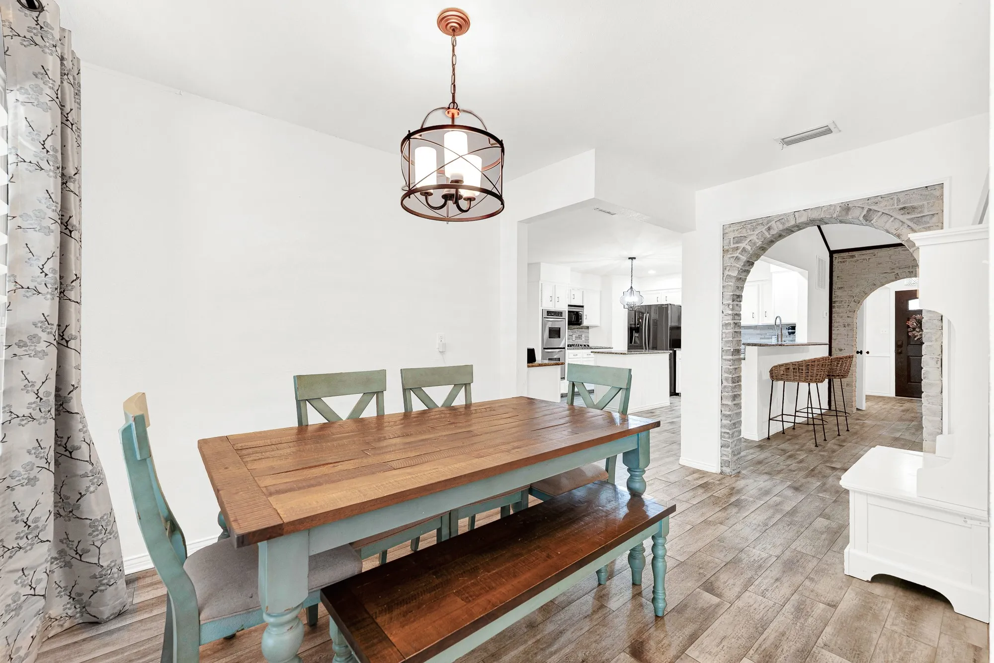 Looking back through the space, this shot showcases the warm pendant lighting, clean white walls, and open view through the brick arch into the main living spaces. It provides a relaxed, cozy atmosphere where family and guests can linger long after dinner is finished.